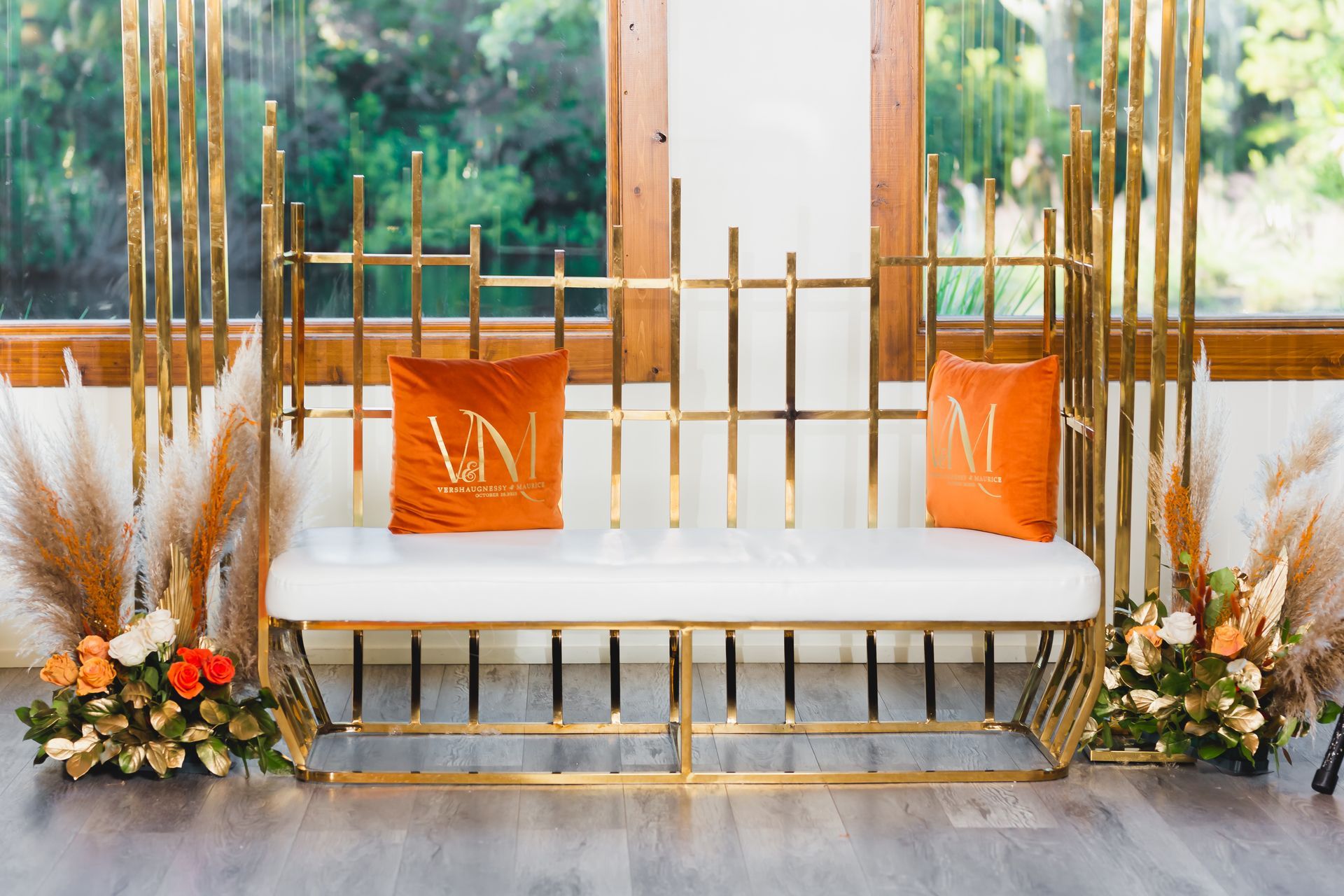 Gold sofa with orange pillows and floral arrangements in a bright indoor wedding-style setting