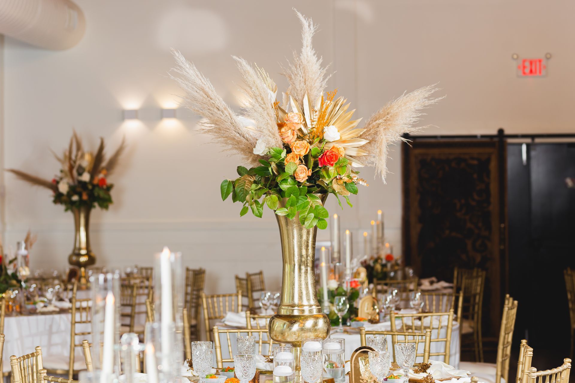 Elegant banquet hall with gold chairs, tall floral centerpieces, and lit candles on round tables