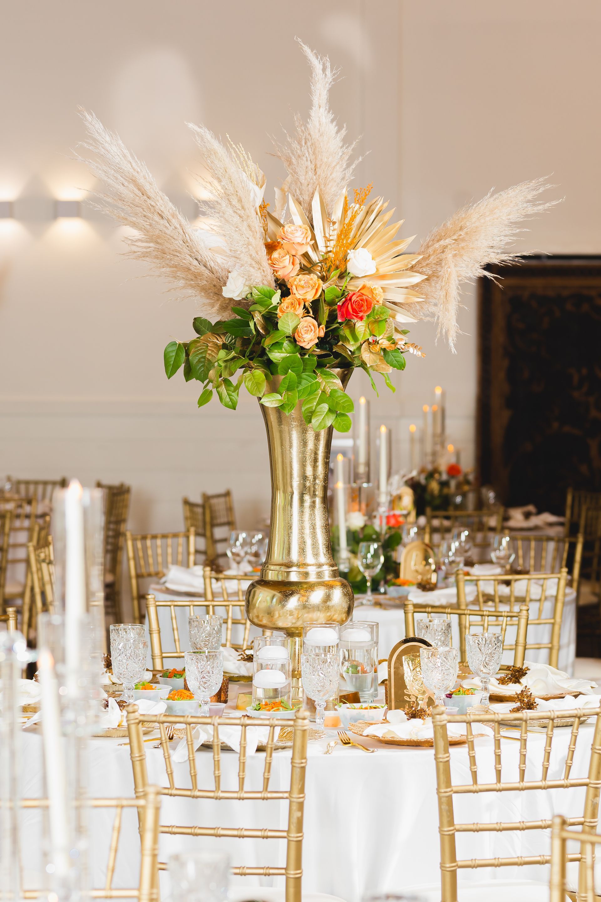 Elegant banquet table with gold chairs, white linens, and a tall floral centerpiece.
