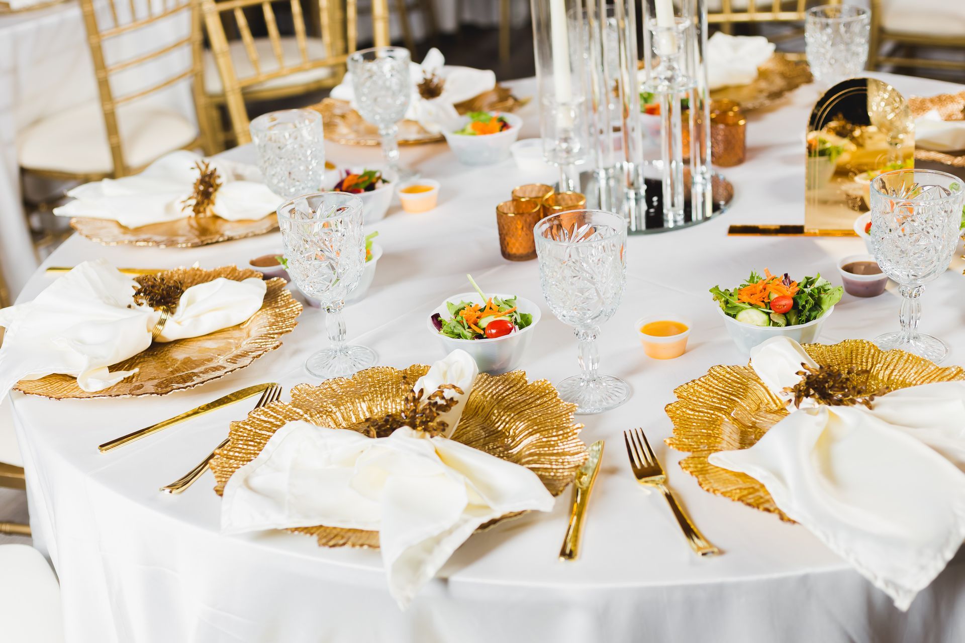 Elegant white and gold banquet table set with plates, glasses, napkins, and floral centerpieces