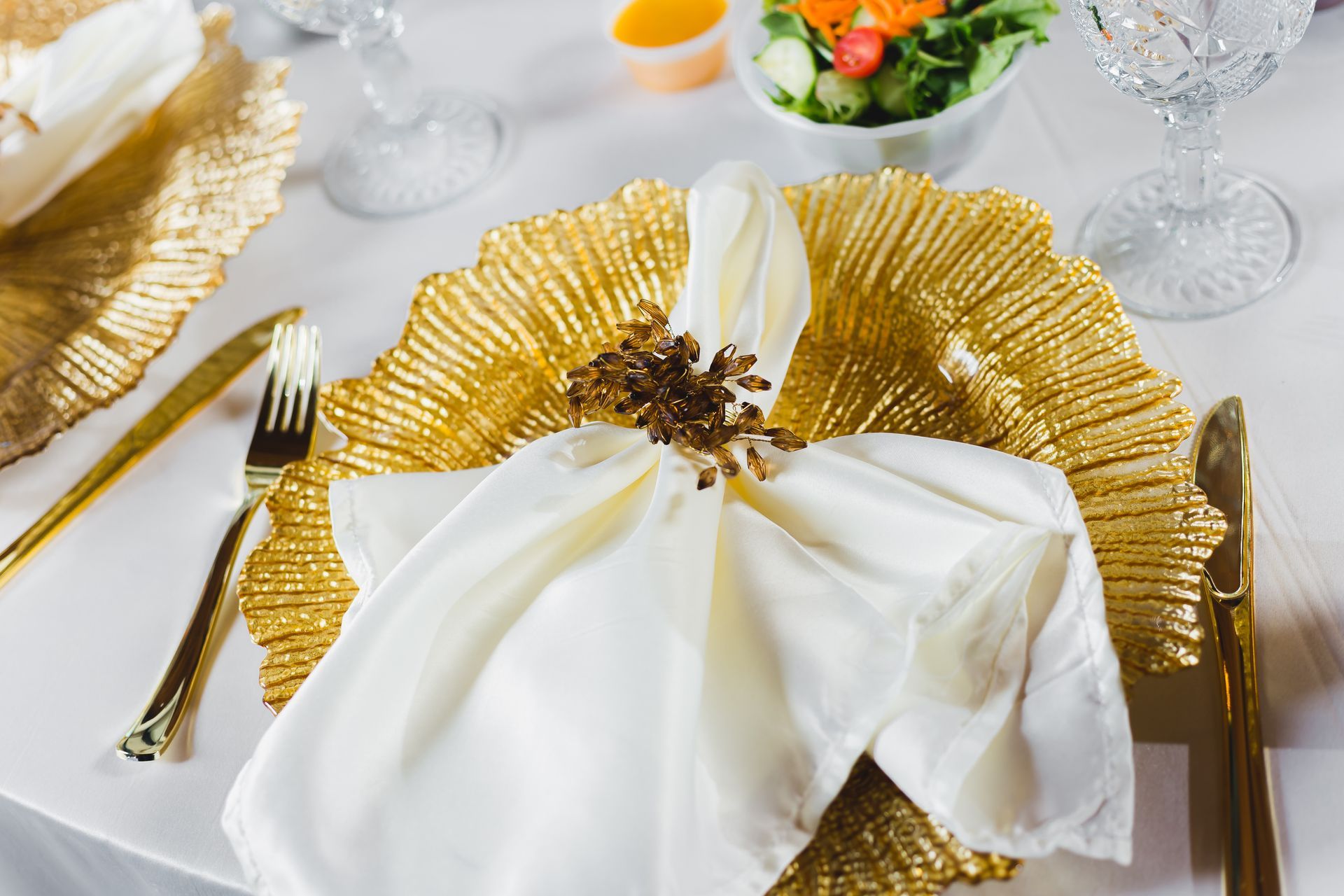 Elegant holiday table setting with white napkins, gold placemats, and glassware on a white tablecloth