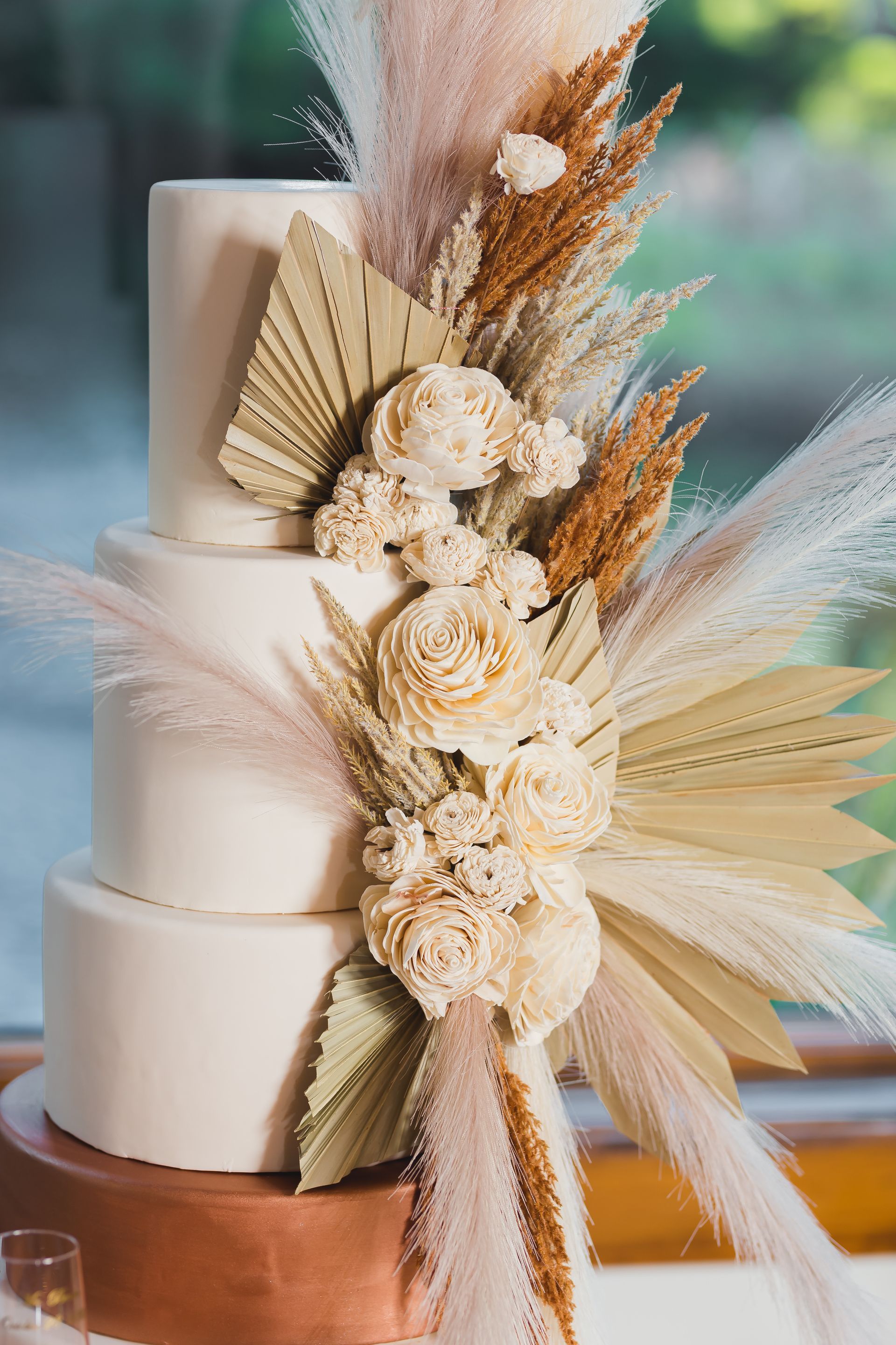 Four-tier white cake with beige dried floral and fan decorations on a wooden stand