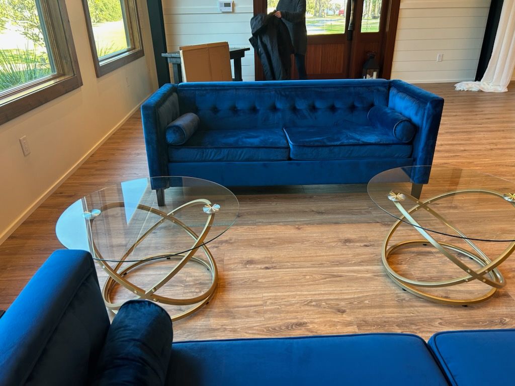Blue sofa and glass coffee tables in a bright sunroom with wood floors.