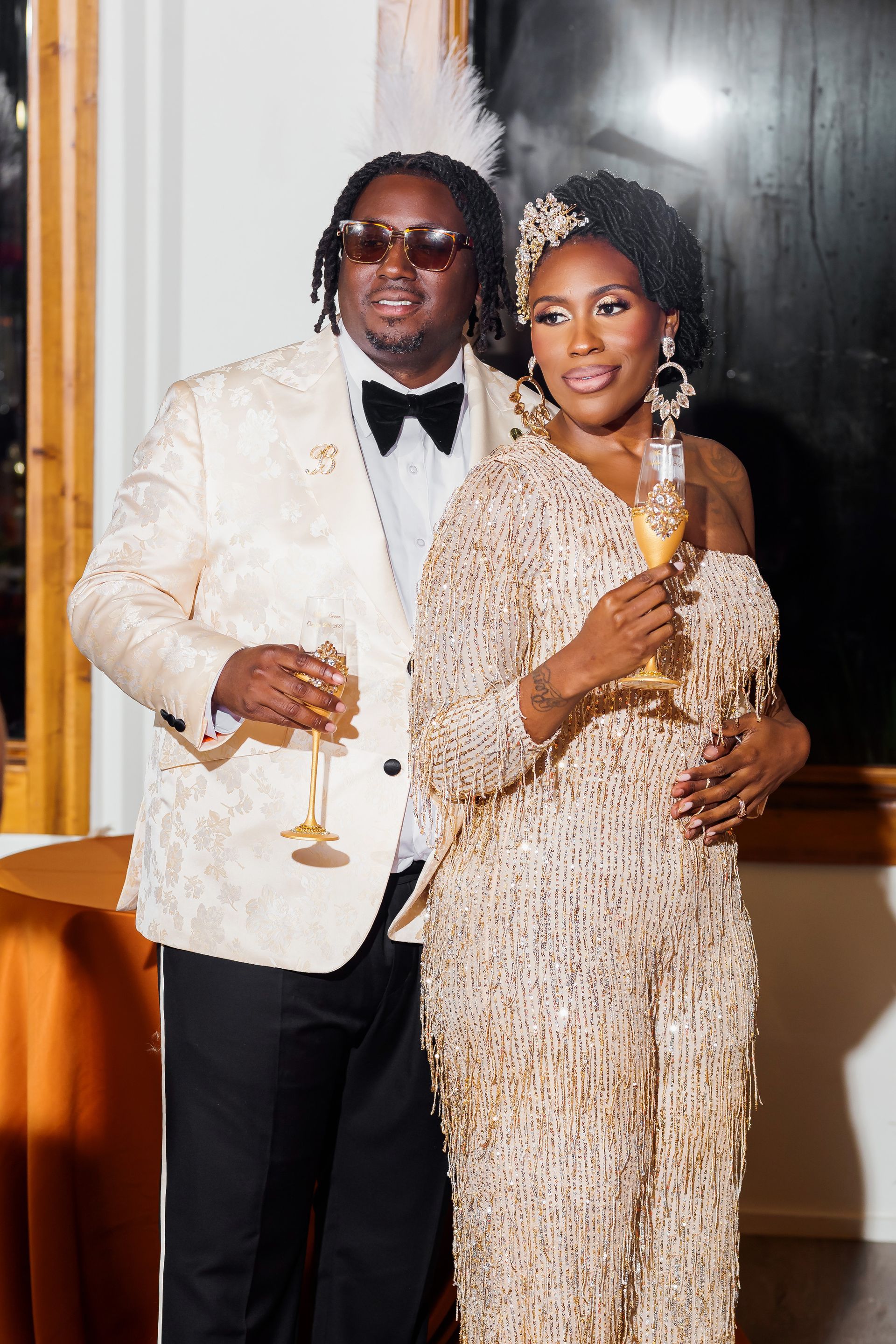 Two people in formal attire smiling and holding champagne glasses at an elegant indoor event.