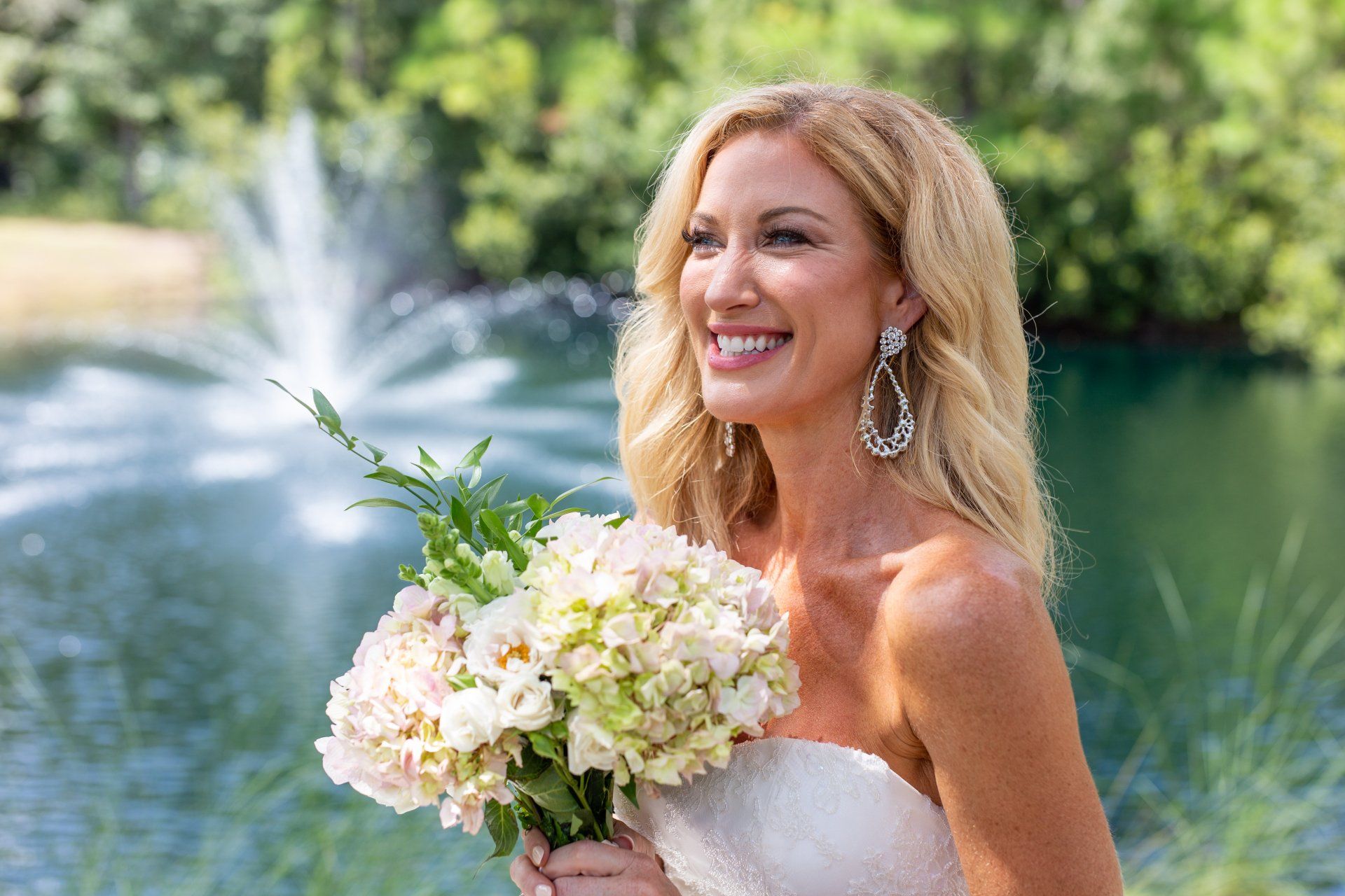 Smiling bride holding a white bouquet by a lake fountain