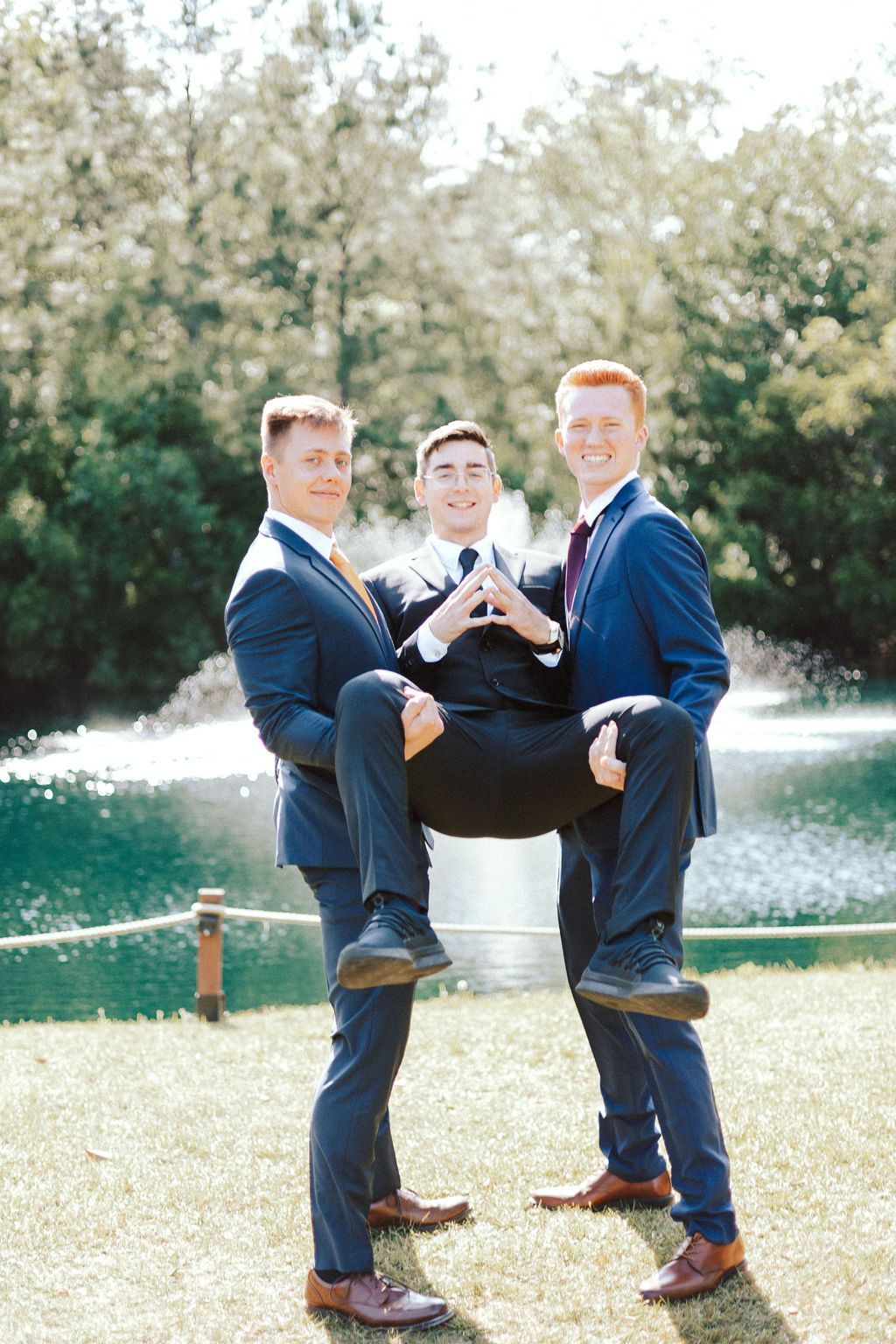 Three men in suits stand in a fountain, with one seated on the shoulders of the other two.
