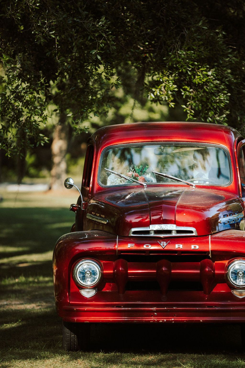 Red vintage pickup truck parked under trees on a grassy road