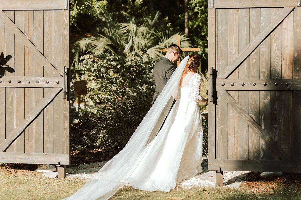 Bride and groom kiss between open barn doors, bride in a long white veil