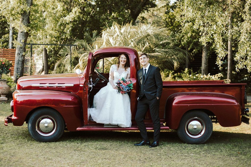 Bride and groom standing by a red vintage pickup truck outdoors