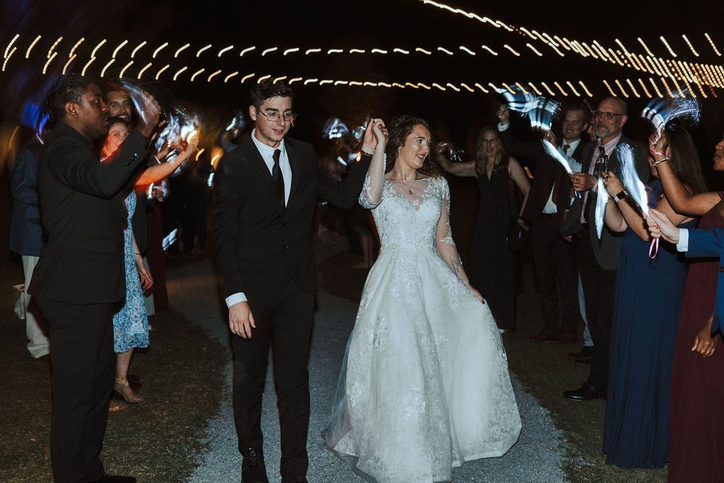 Bride and groom walking through cheering guests with sparklers at a nighttime wedding send-off