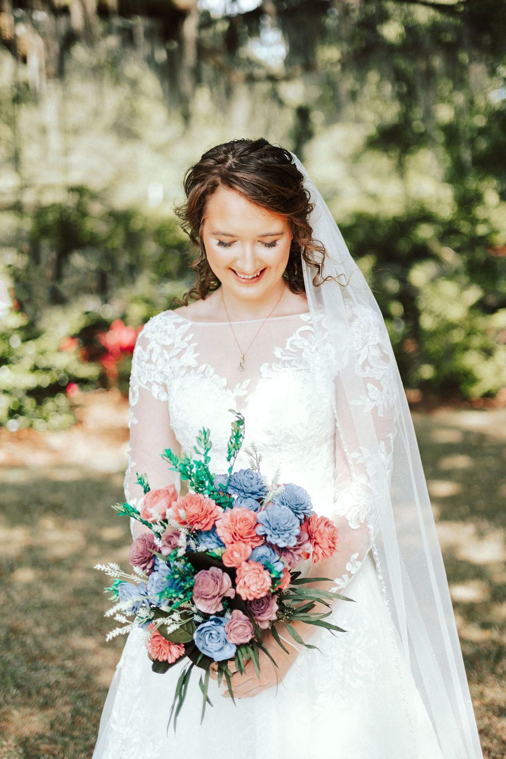 Bride holding a colorful bouquet, wearing a white dress and veil outdoors in a garden