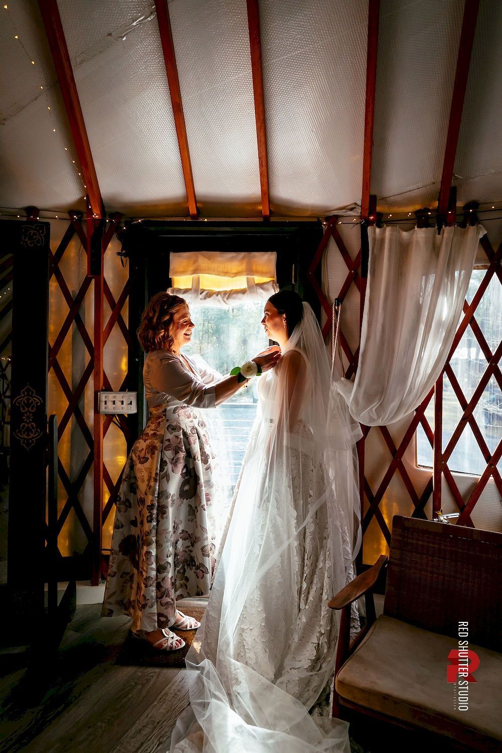 Two people in a tent-like room adjust a sheer white curtain near a bright doorway.