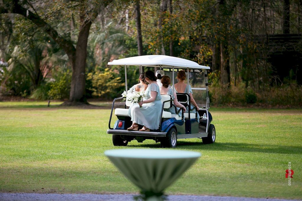 People riding a golf cart across a grassy park under trees