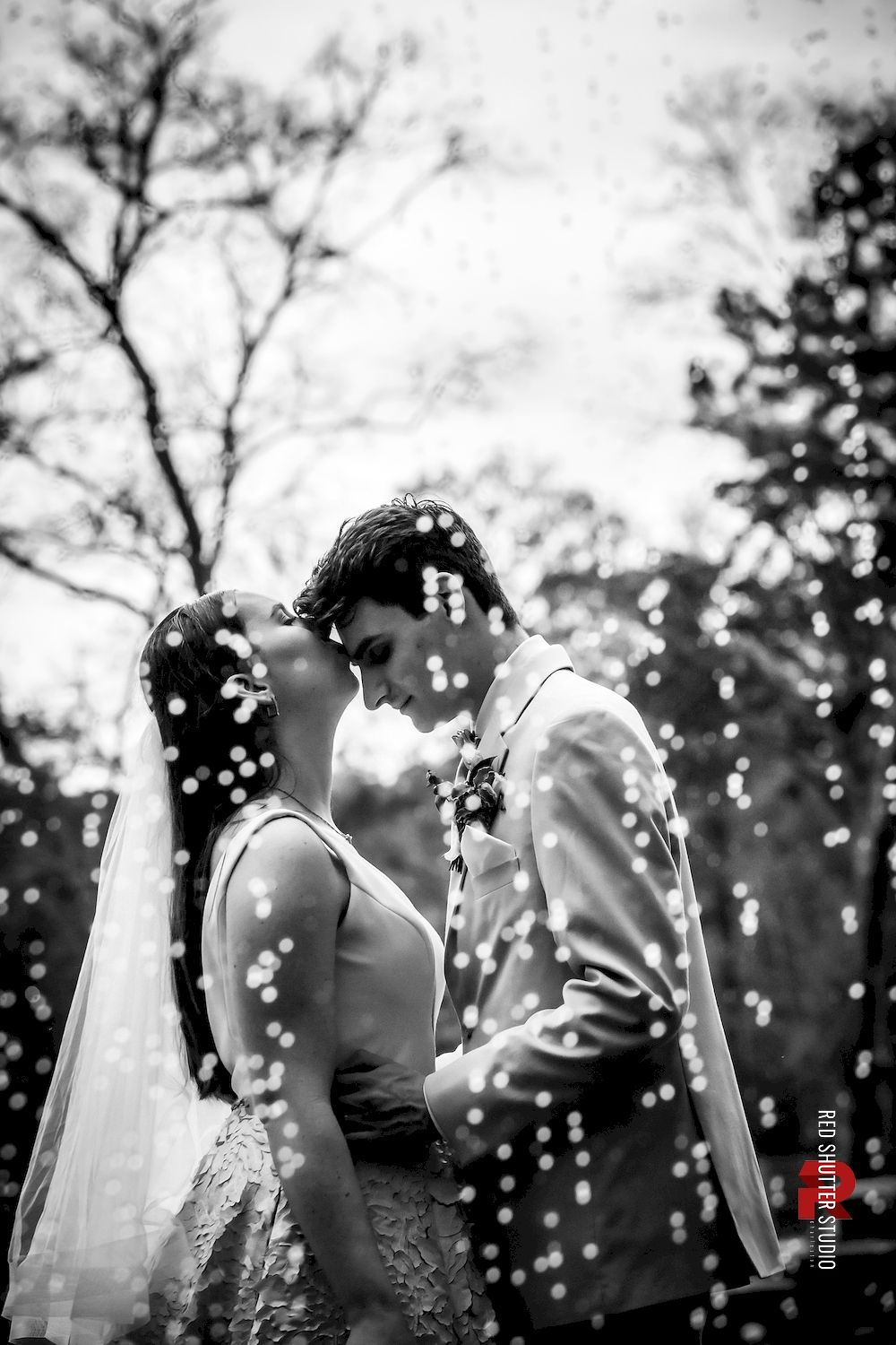 Bride and groom standing close outdoors, touching foreheads in a snowy black-and-white portrait.