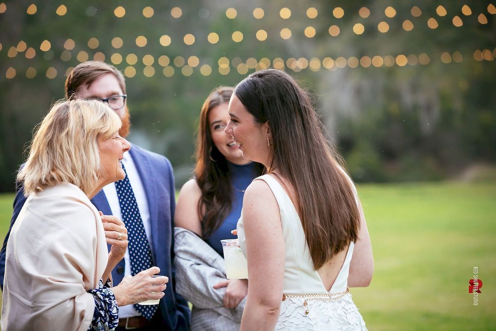 Four people chatting outdoors at a garden event, with string lights softly glowing in the background.