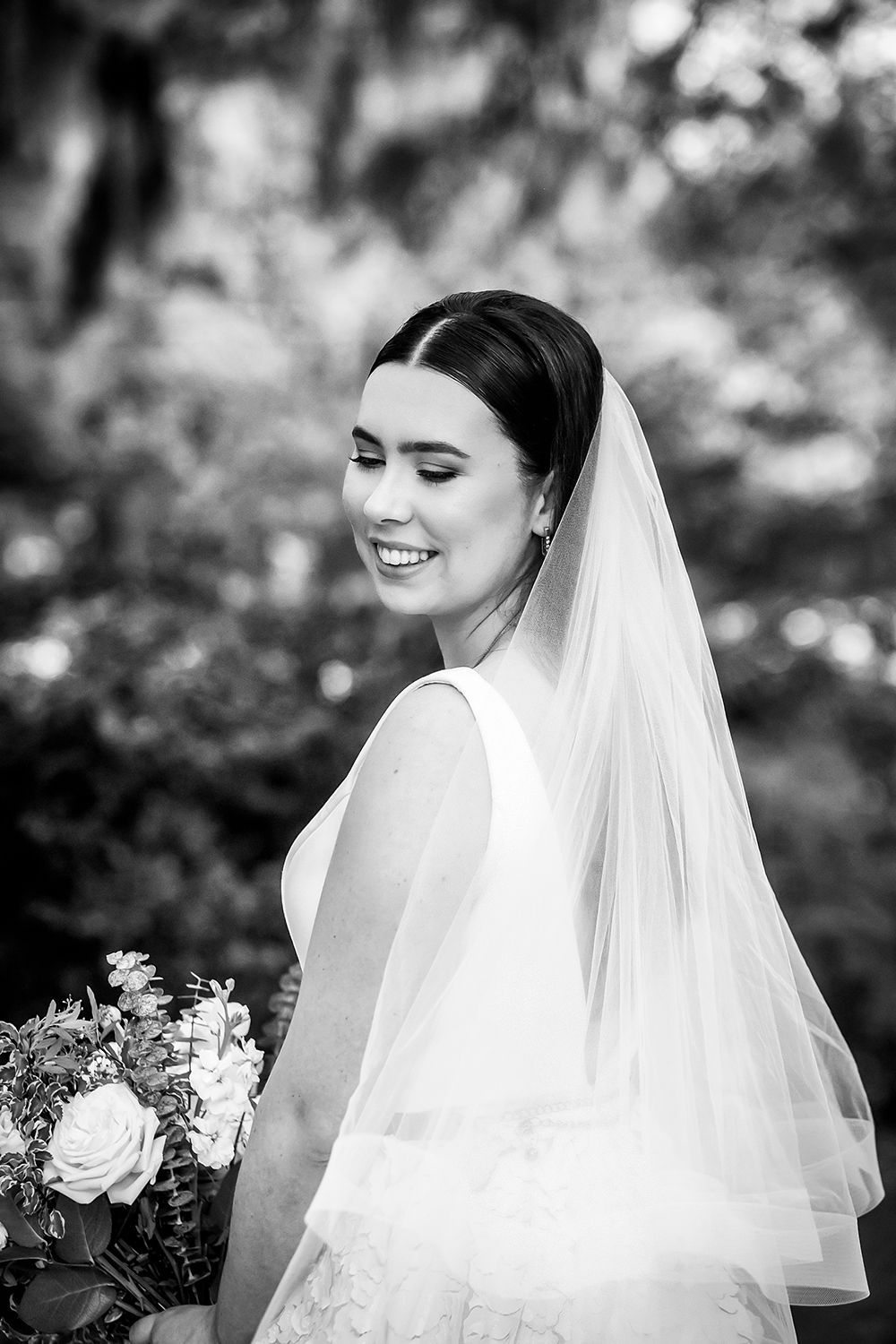 Bridal portrait of a smiling woman in a veil holding a bouquet outdoors