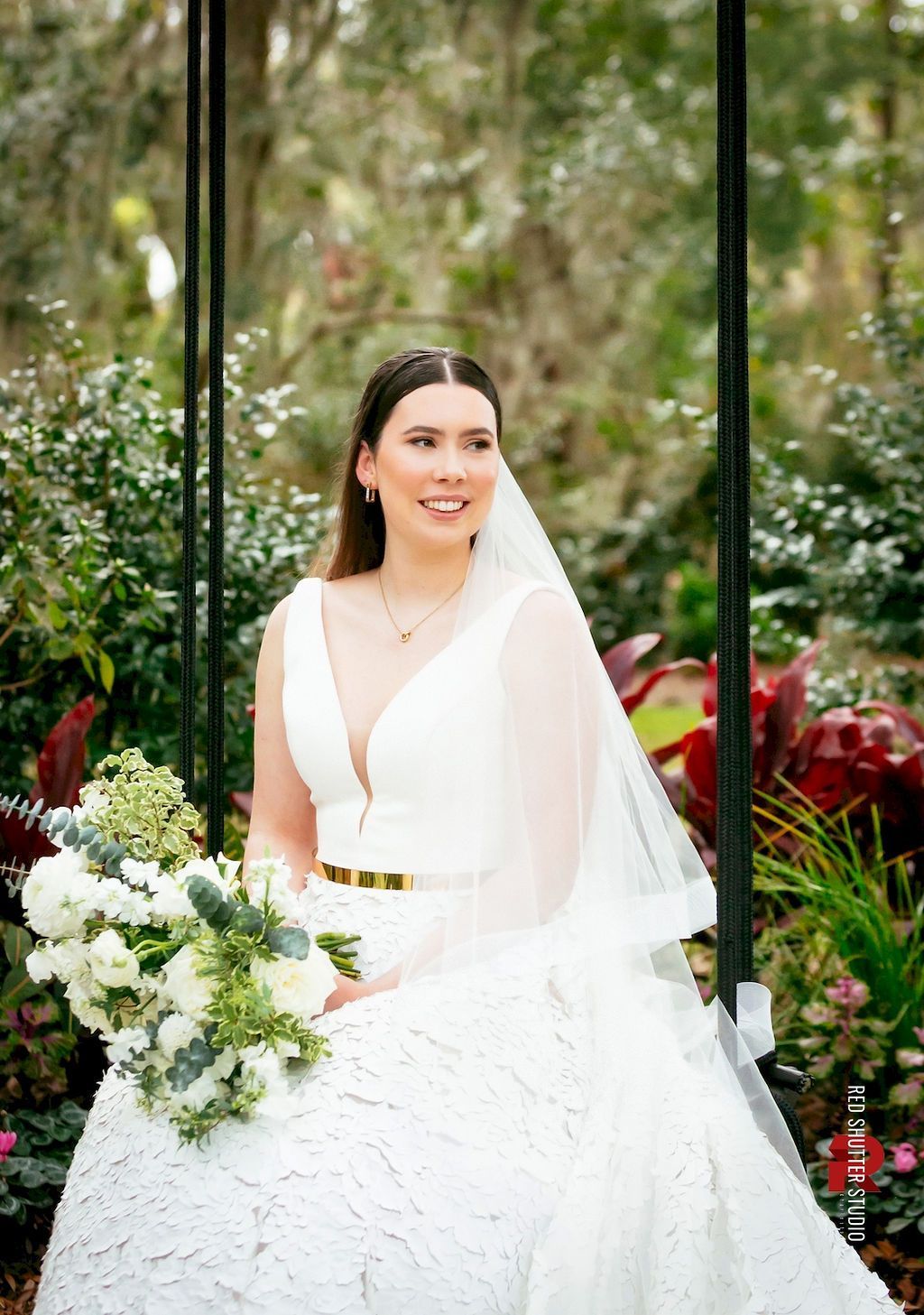 Bride in a white gown and veil holding a bouquet in a garden setting