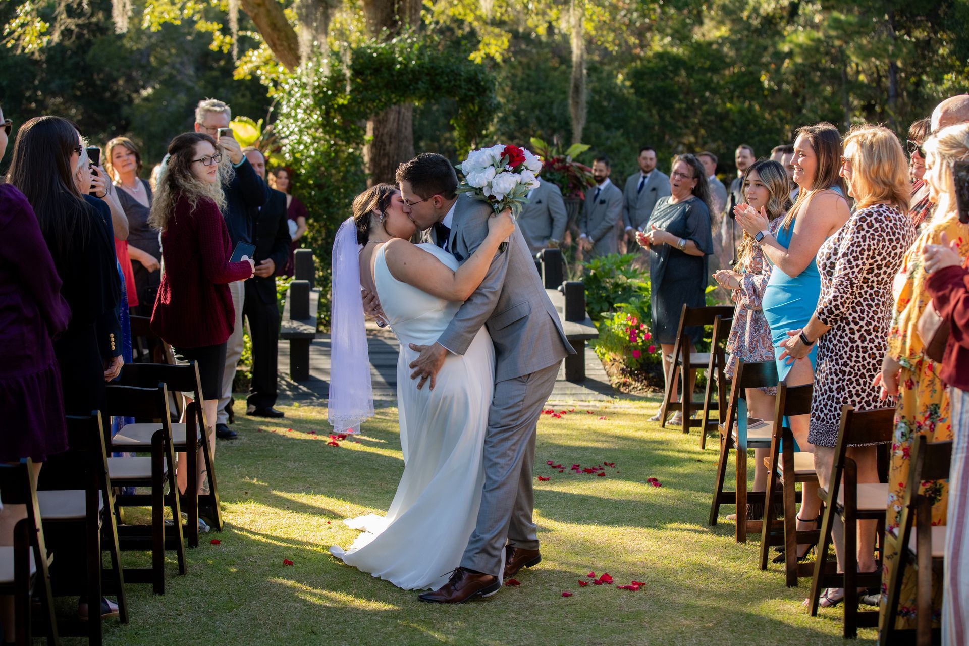 Bride and groom kissing on an outdoor wedding aisle lined with seated guests and flowers