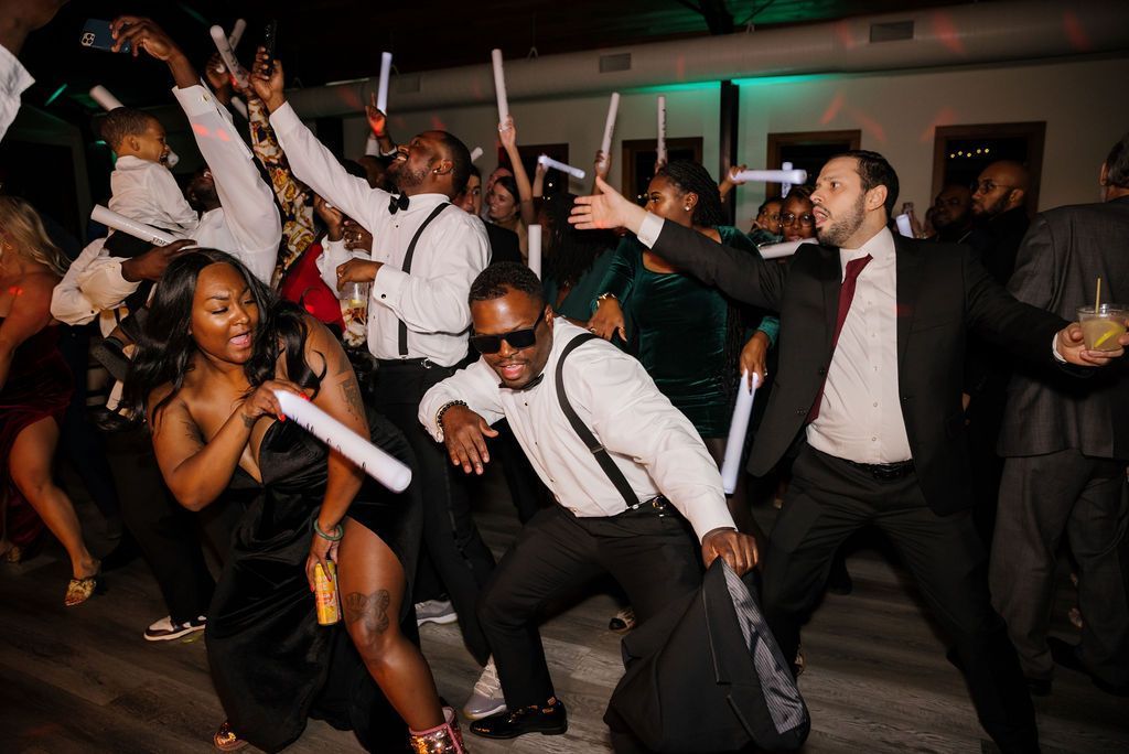 People dancing at a lively party, smiling and holding white glow sticks under colorful lights