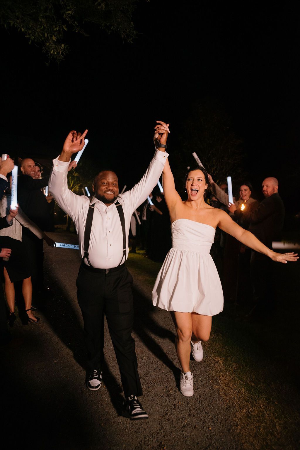 Two people dancing and cheering outdoors at night, with others in the background
