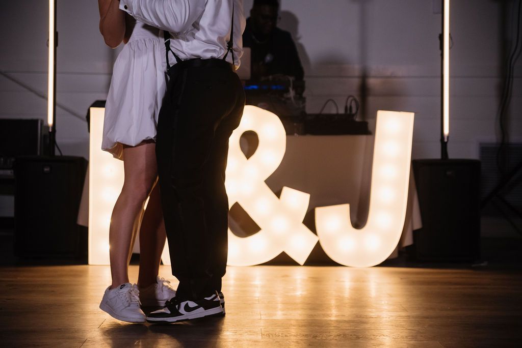 Couple dancing in front of glowing “& J” letters on a stage