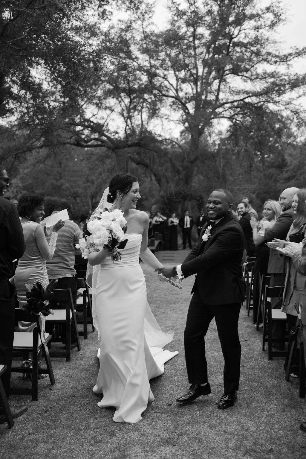 Bride and groom dancing outdoors at a wedding ceremony, guests seated around them.