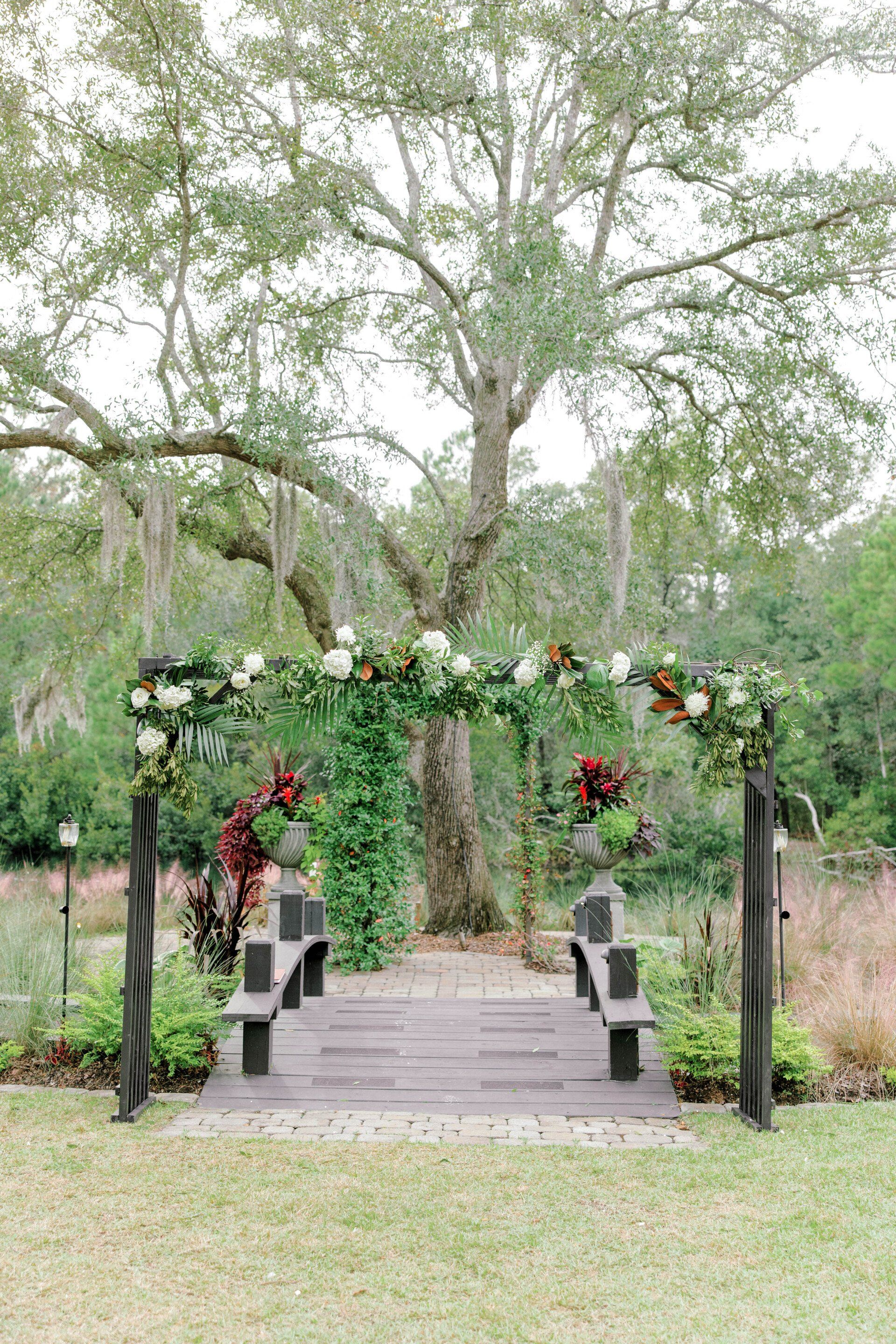 Flower-decorated wooden arch over a garden walkway with trees and greenery beyond