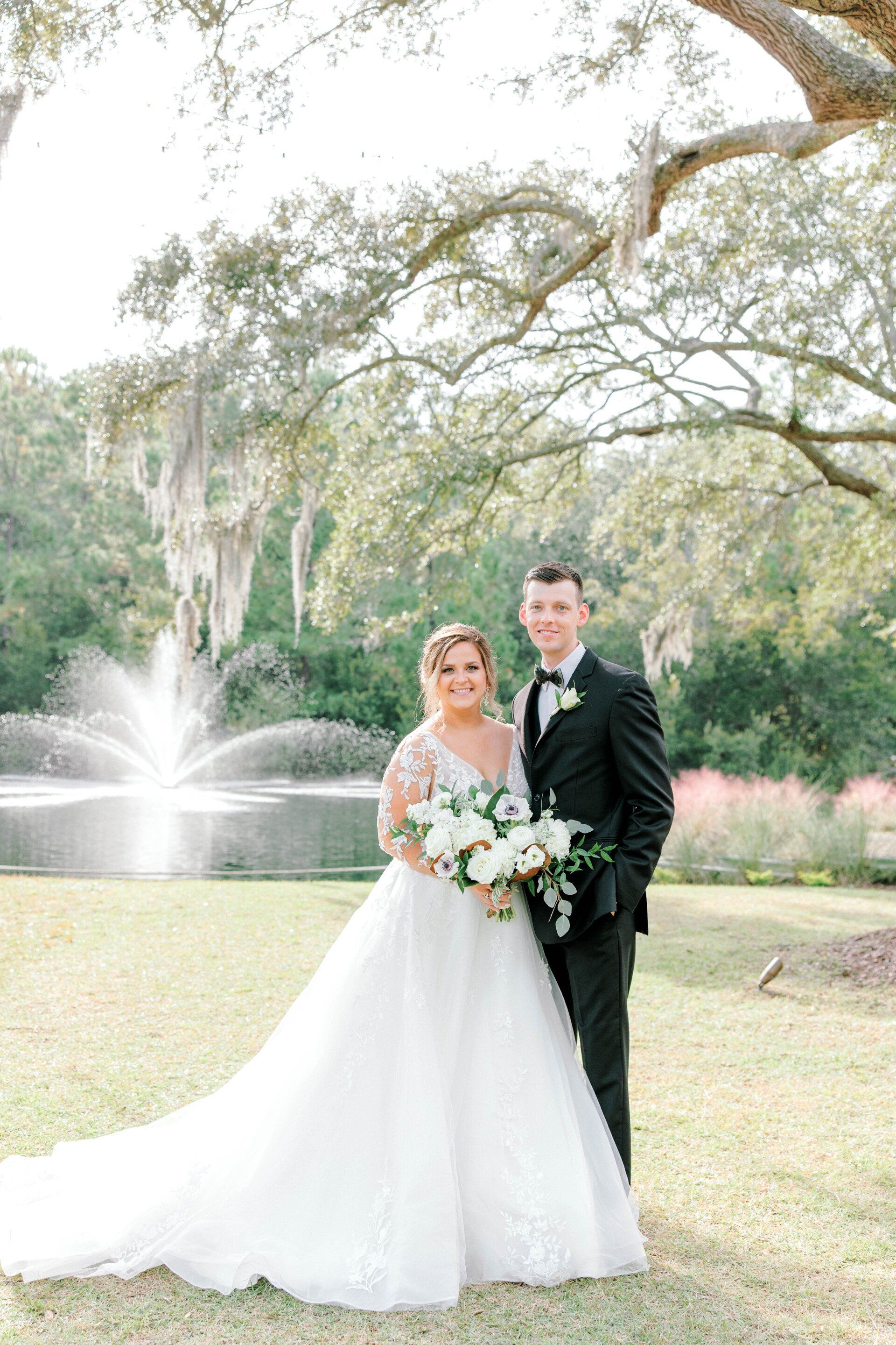 Bride and groom in a garden by a fountain, holding a bouquet and smiling