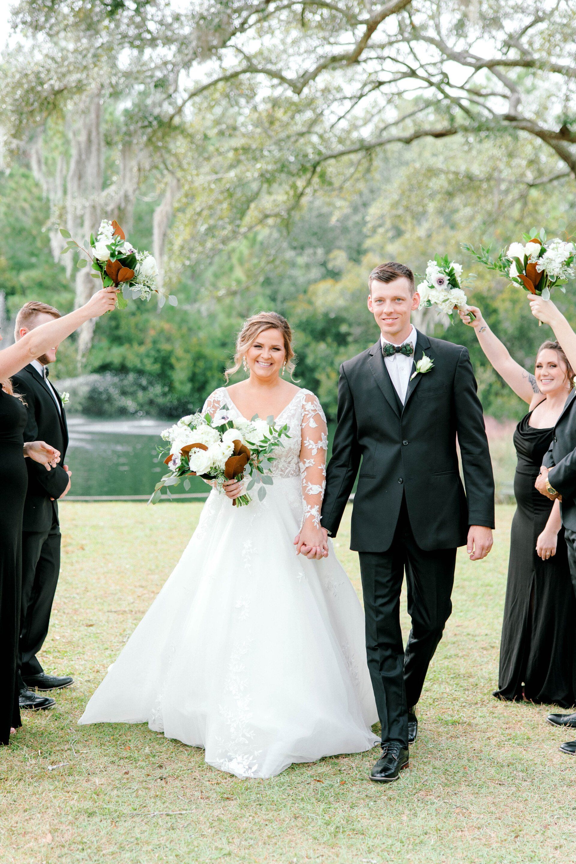 Bride and groom walking outdoors under raised bouquets at a wedding ceremony