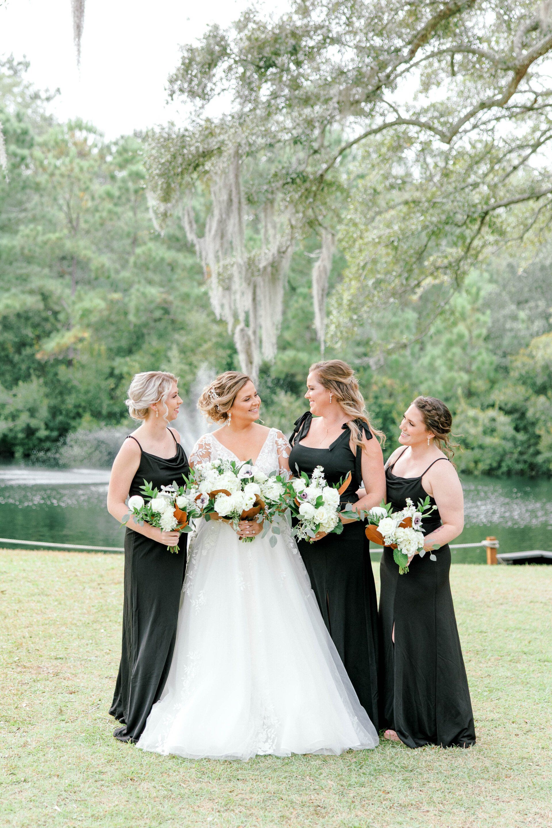 Bride with three bridesmaids holding bouquets outdoors under trees.