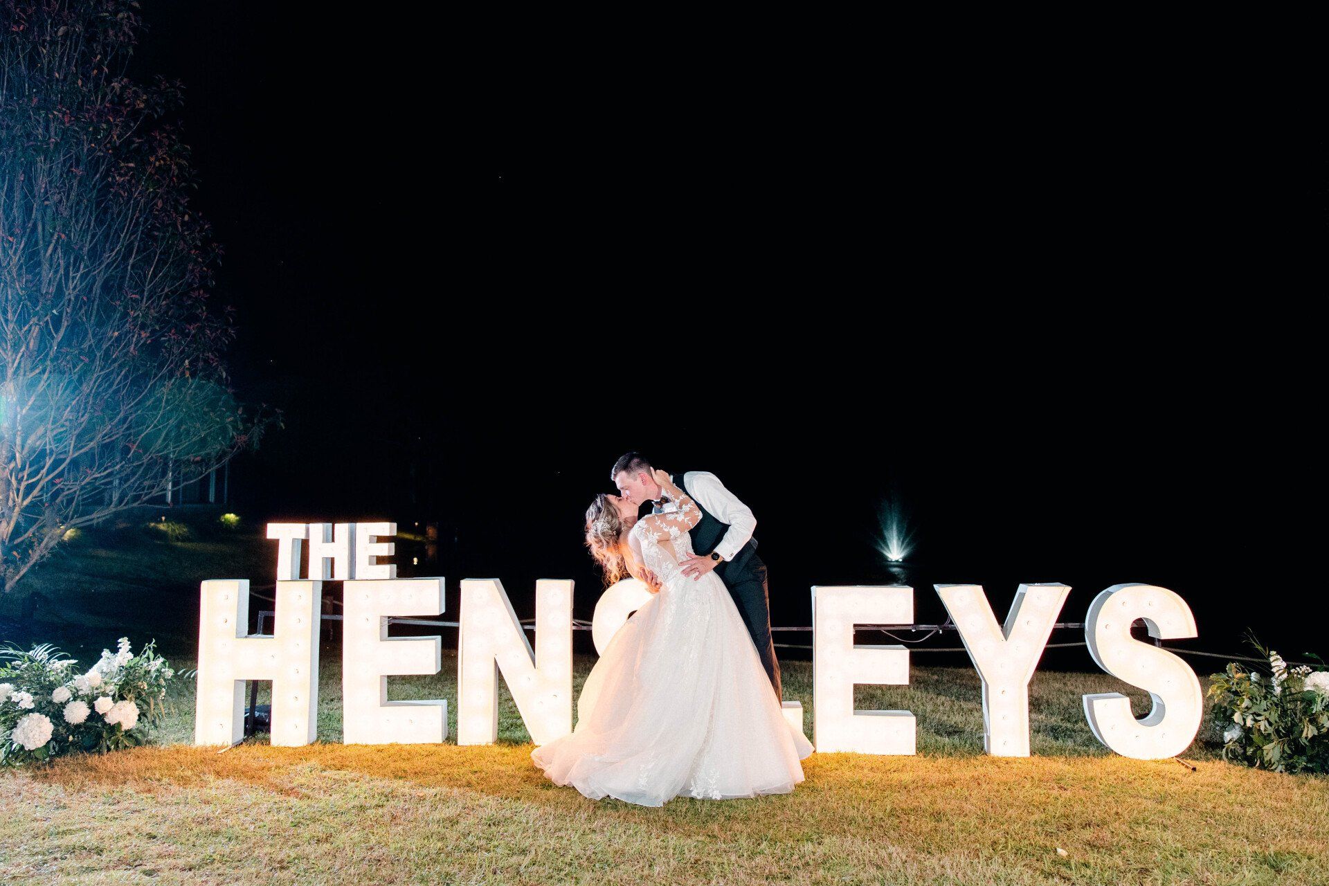 Bride and groom standing beside large lit “THE HENDEYS” letters at night