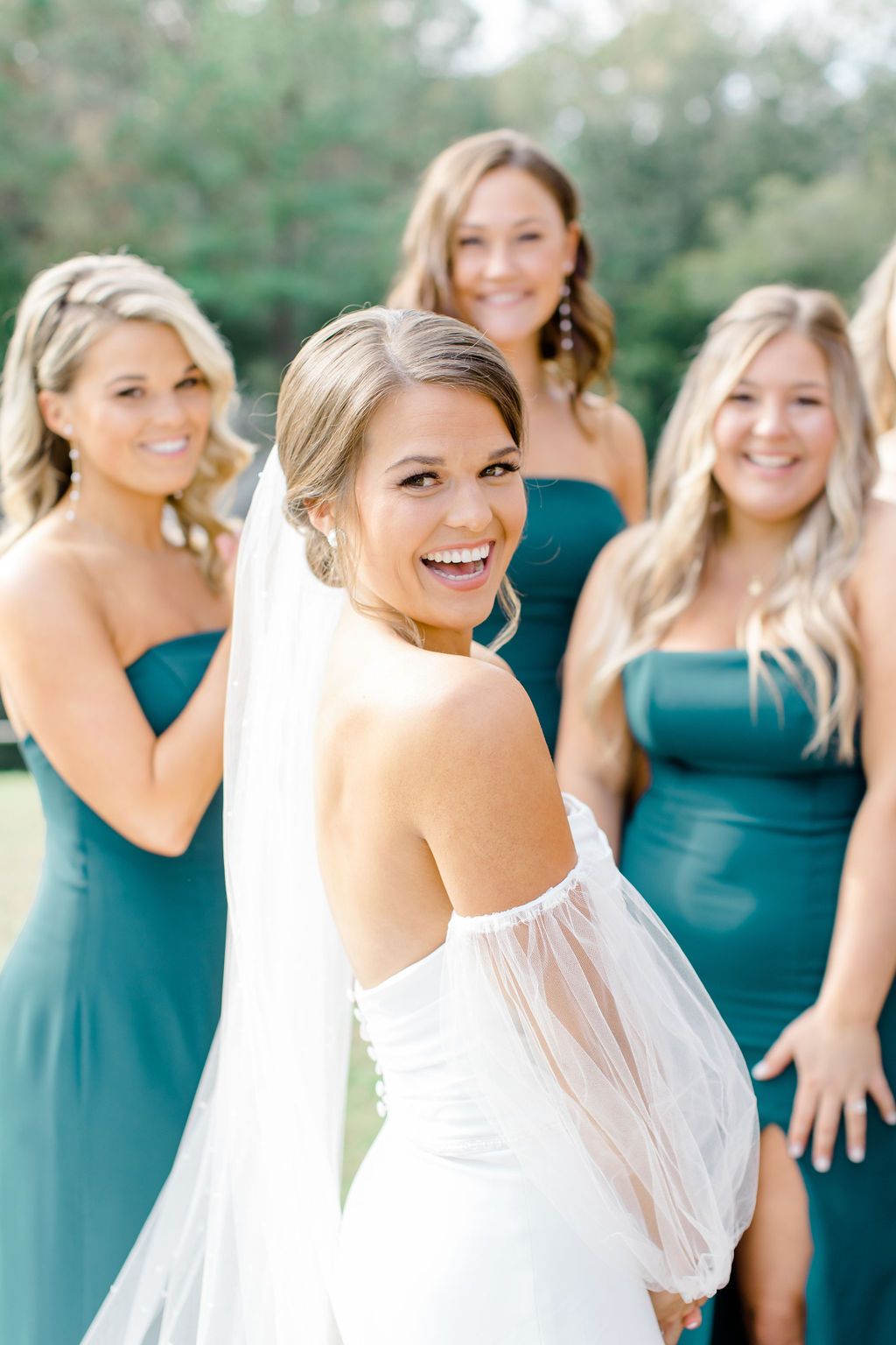 Bride in white dress smiling with four bridesmaids in teal dresses outdoors