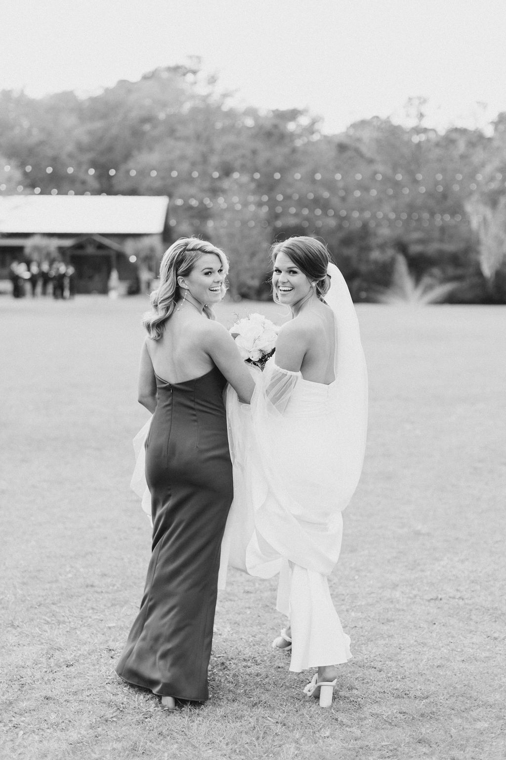 Two women in dresses smiling and holding hands outdoors on a grassy field