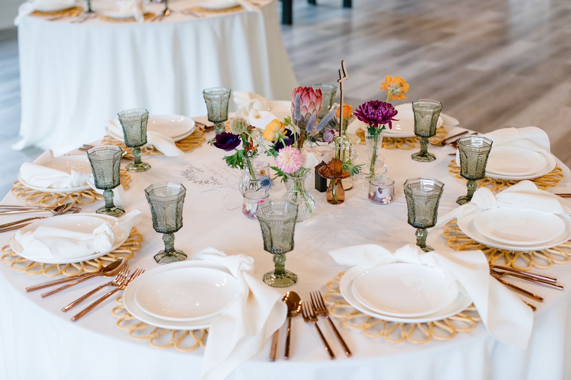 Elegant round banquet table set with white plates, gold cutlery, glassware, and a floral centerpiece