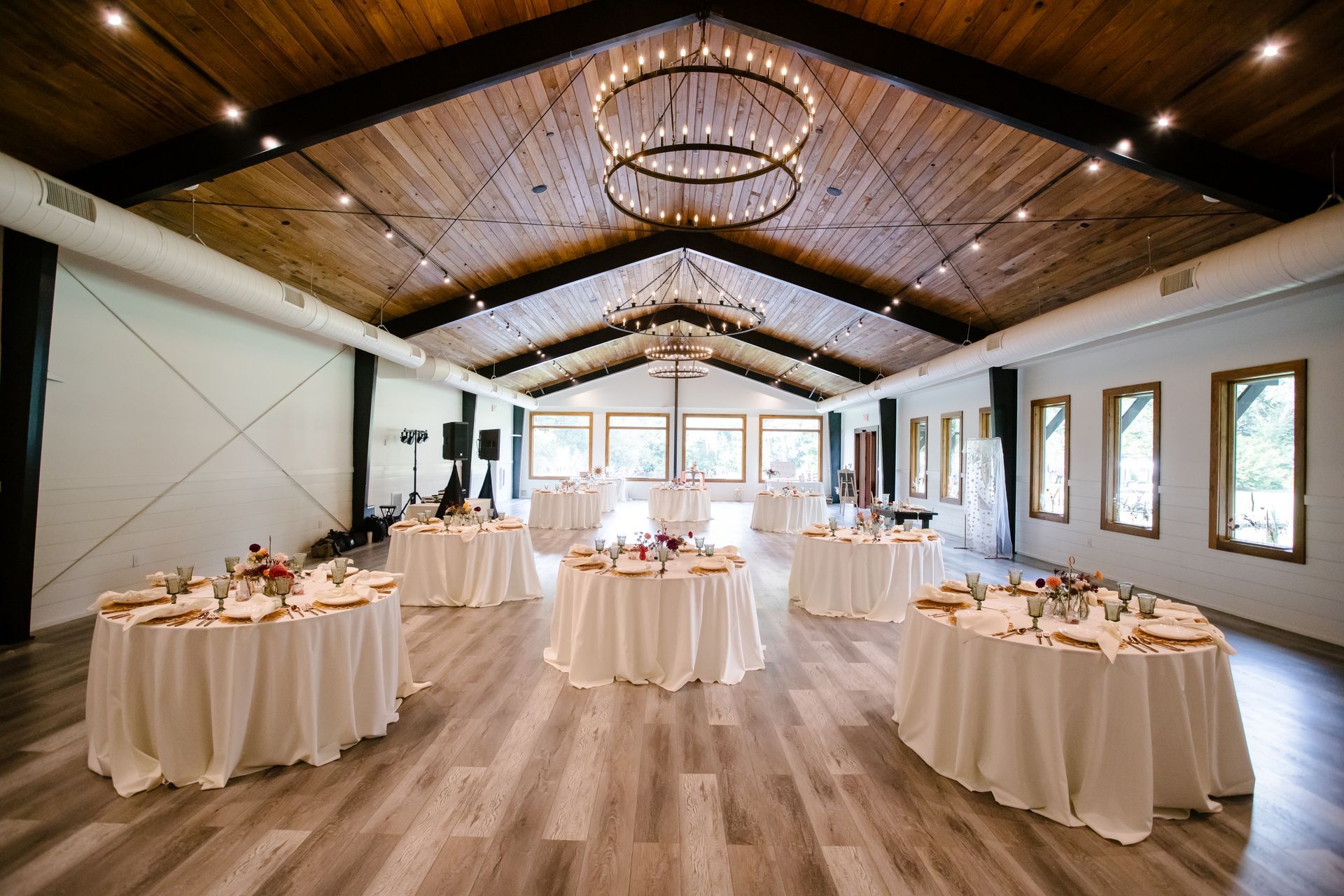 Elegant banquet hall with round tables, white linens, and chandeliers under a vaulted wood ceiling