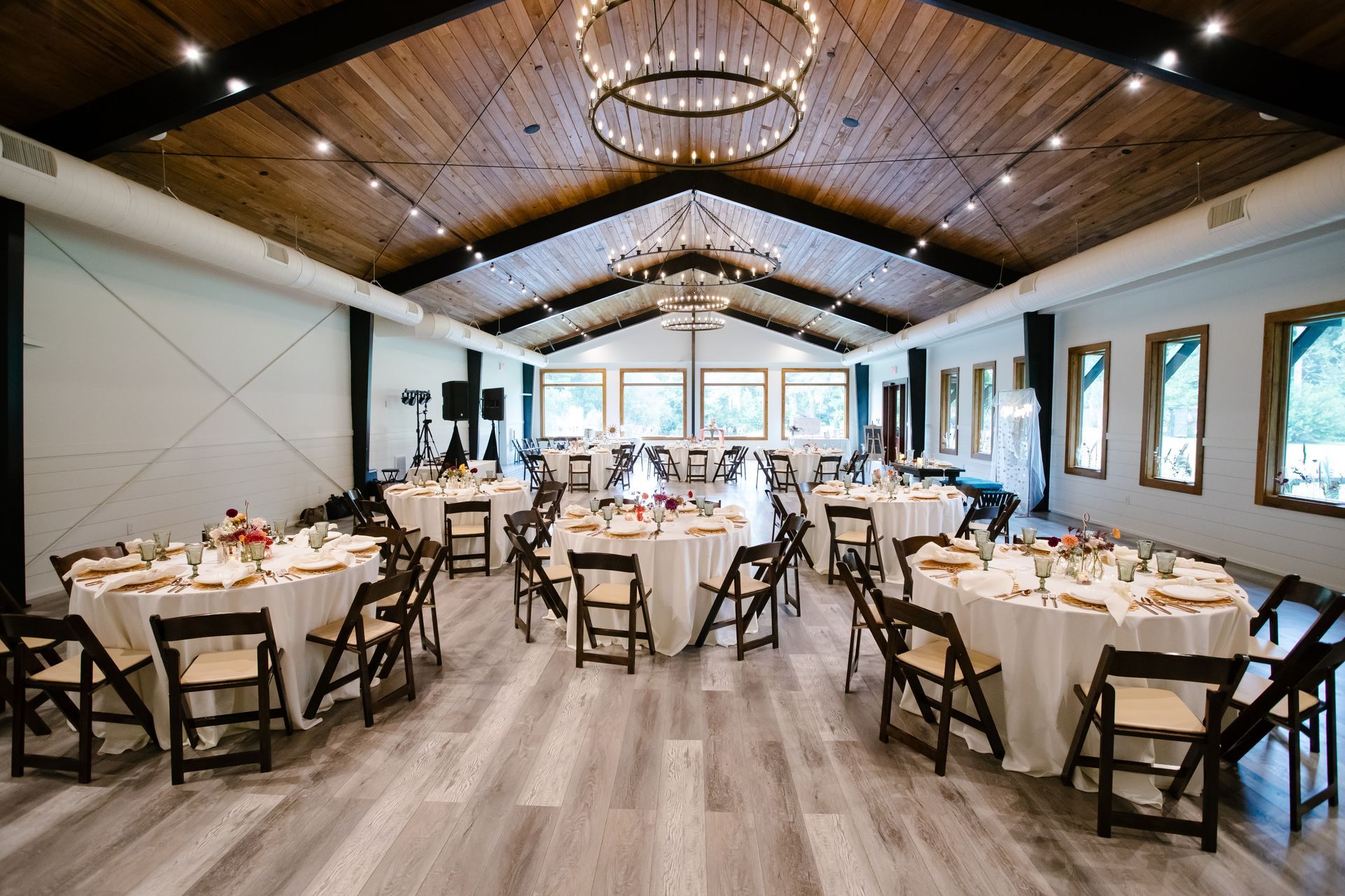 Rustic banquet hall with round tables set for a formal event and wooden chairs under a vaulted ceiling