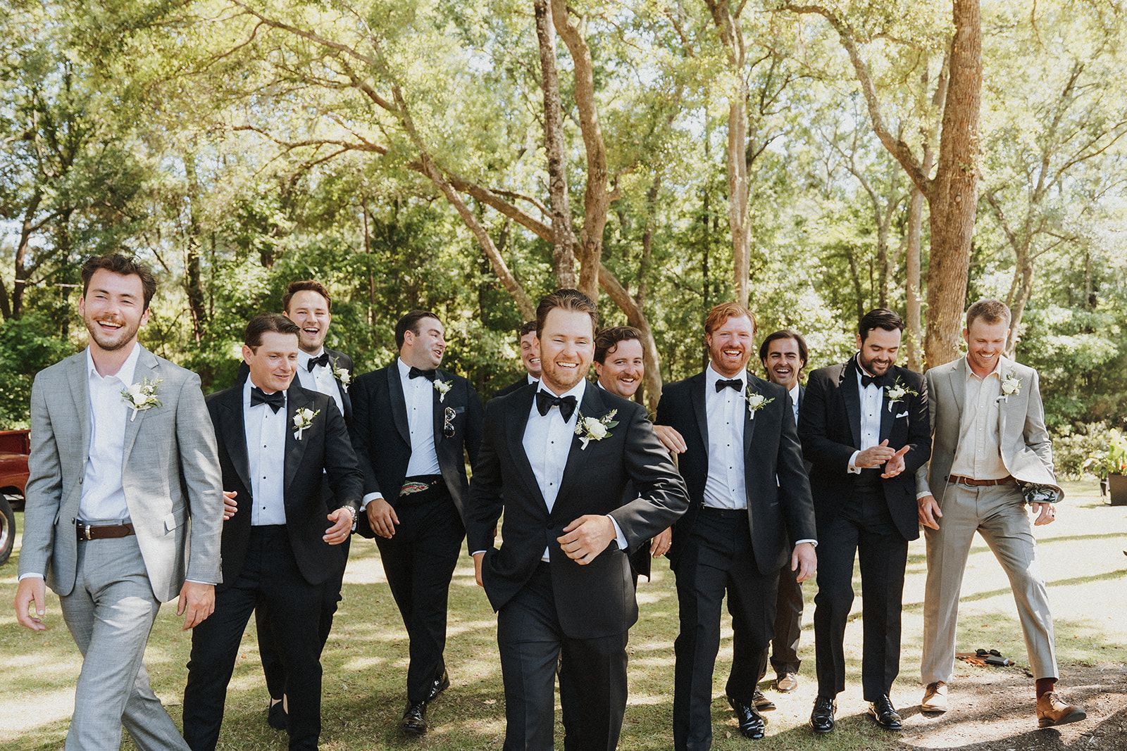 Group of men in suits walking outdoors on a tree-lined path at a formal event