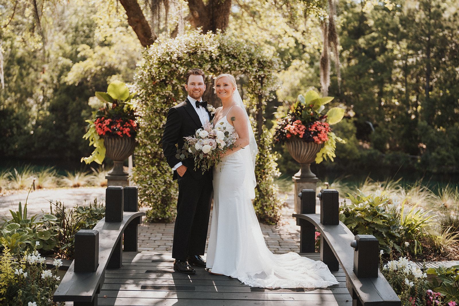 Bride and groom standing on an outdoor wedding aisle surrounded by flowers and trees