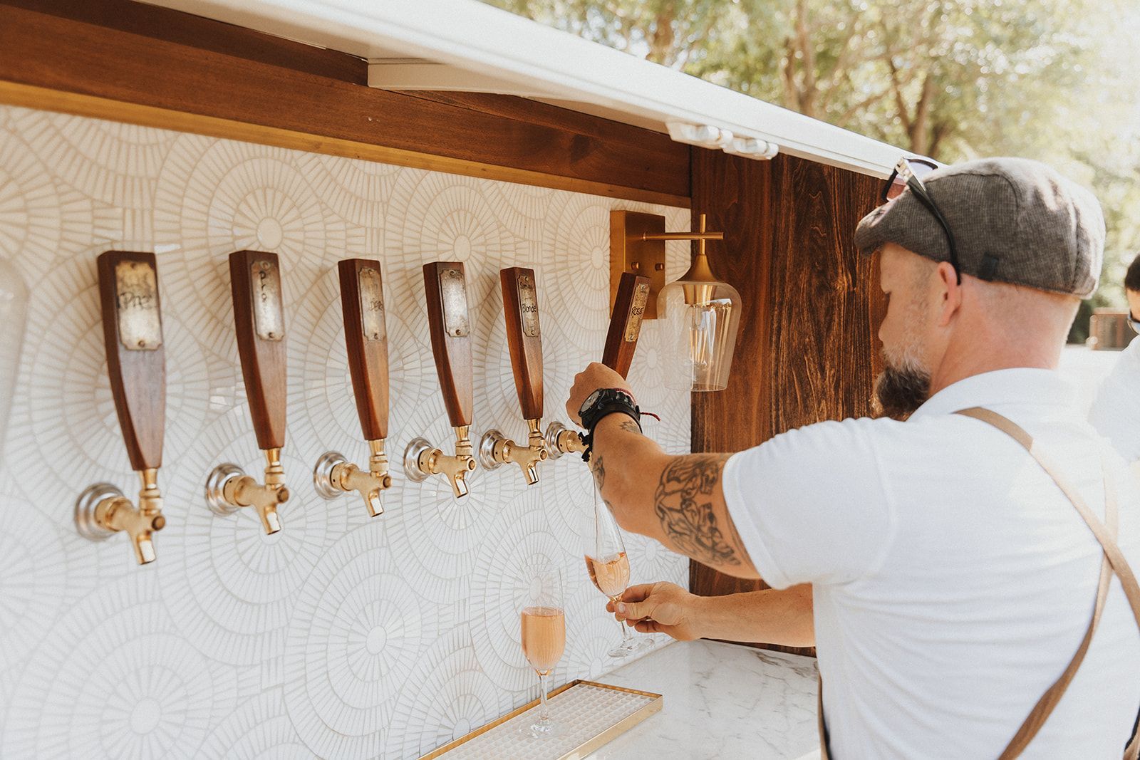 Man taps wooden beer taps at an outdoor bar with white tenting and string lights