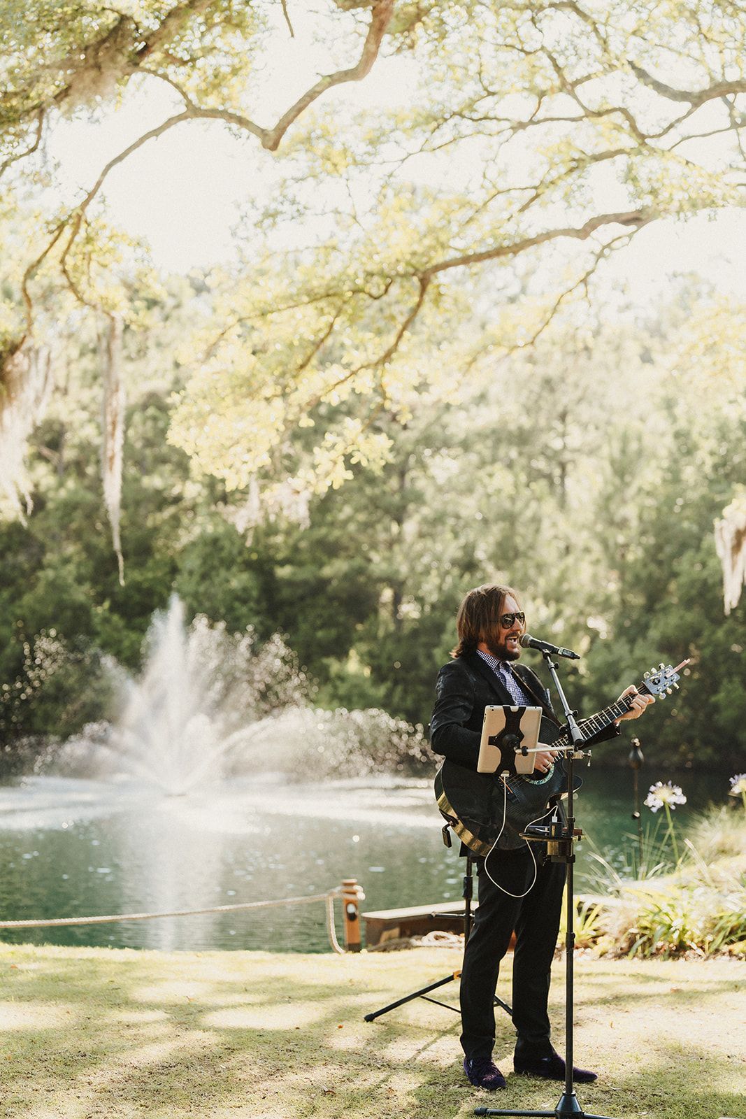 Musician playing guitar beside a lake and fountain in a sunlit park