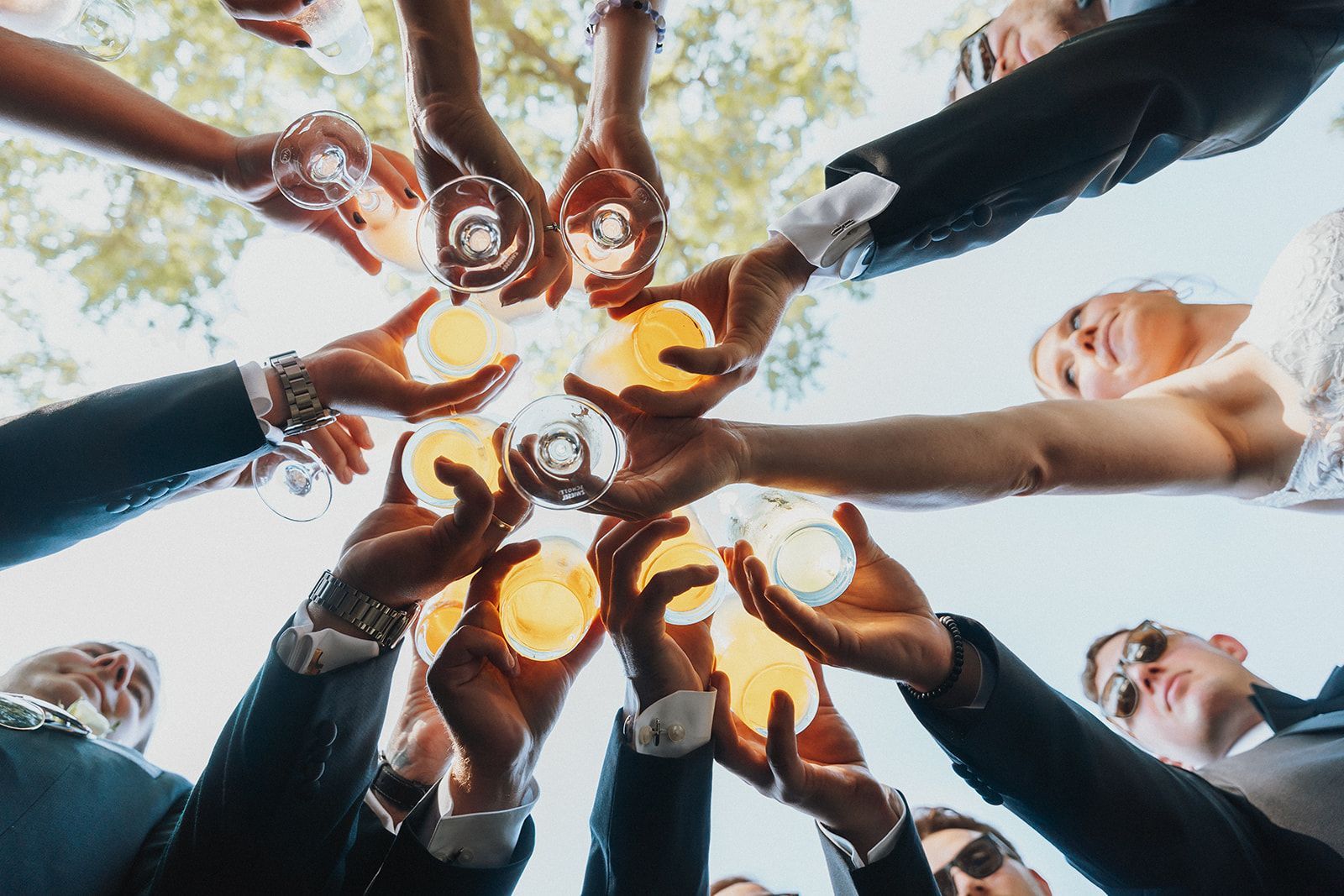 Friends raising glasses in a circle for a toast outdoors, seen from below.