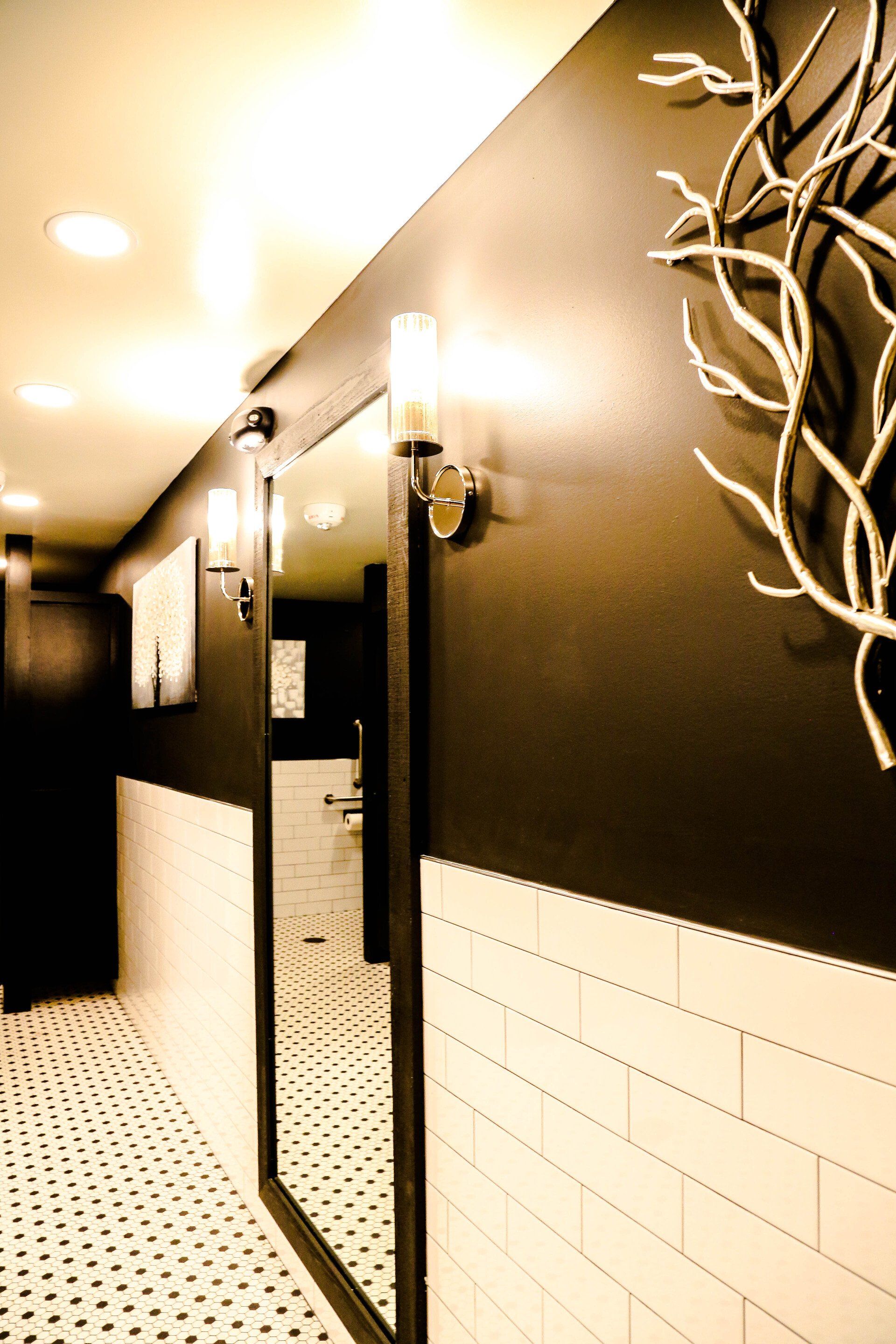 Modern bathroom interior with a large mirror, black-and-white tile, and decorative wall branches