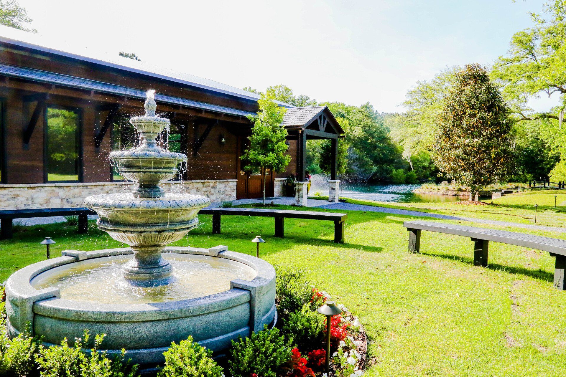 Stone fountain in a sunny garden beside a brick building and green lawn