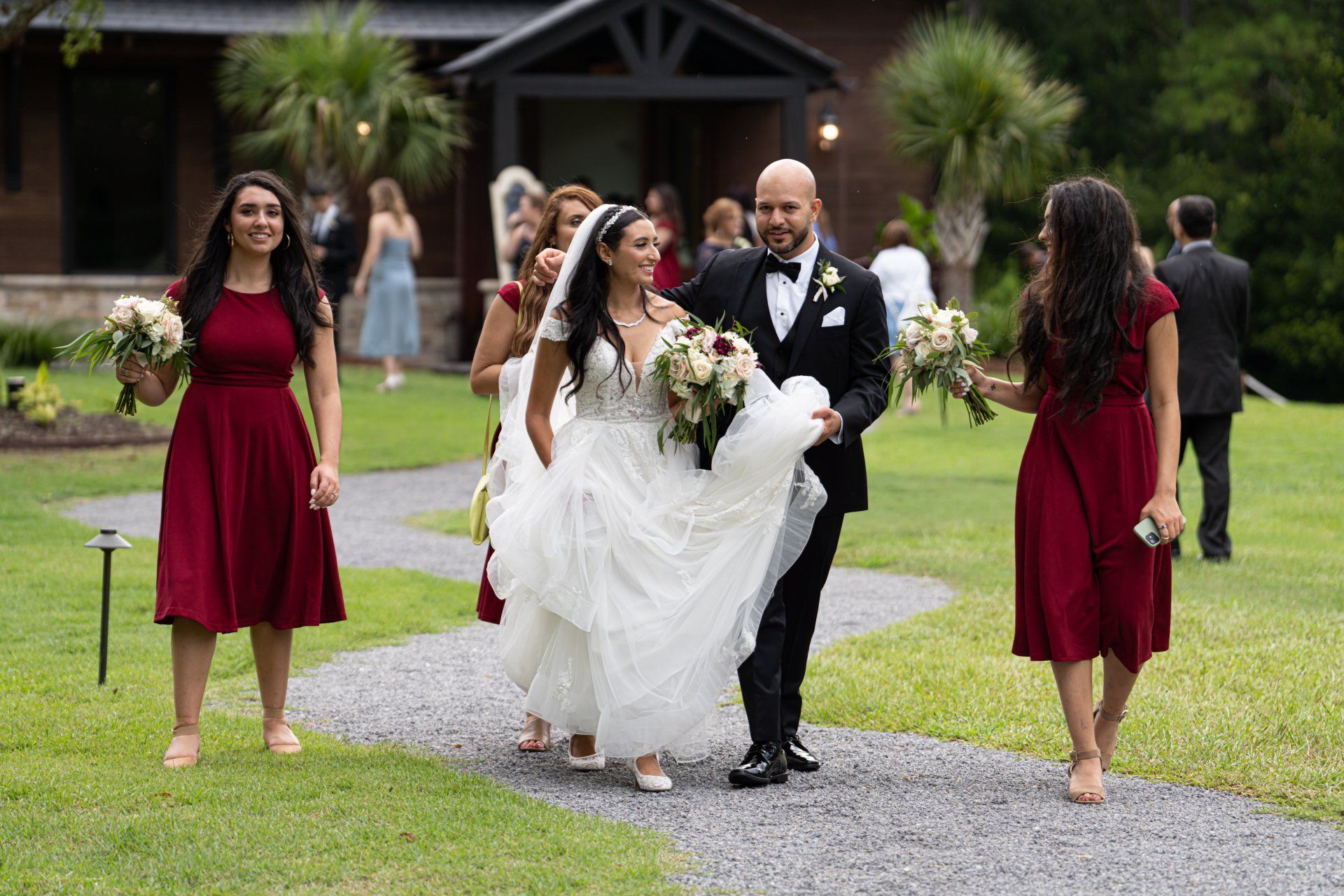 Wedding party walking on a gravel path, with the bride in a white dress and groom in a black tuxedo.
