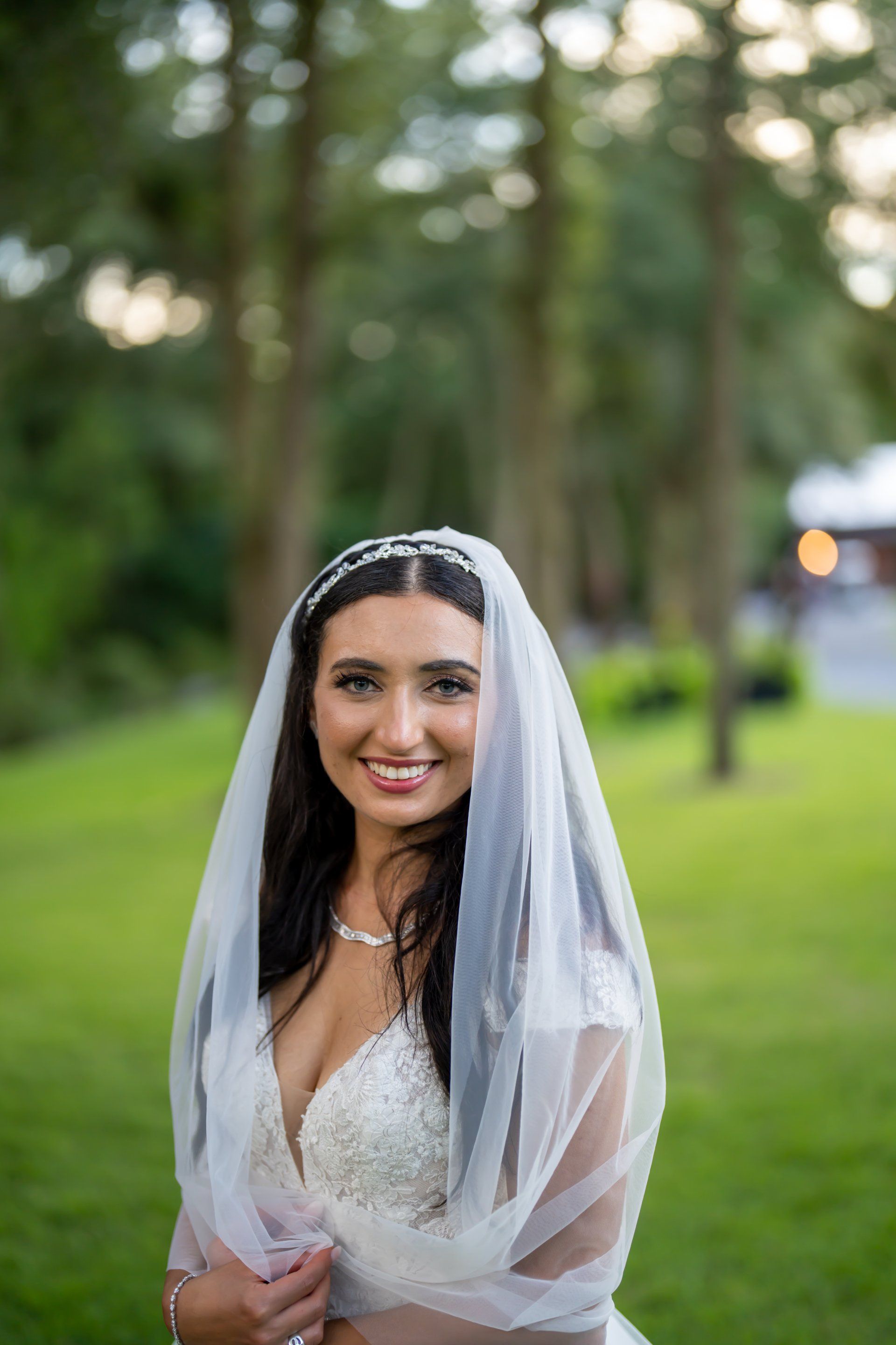 Smiling bride in a white veil and dress standing outdoors in a green park