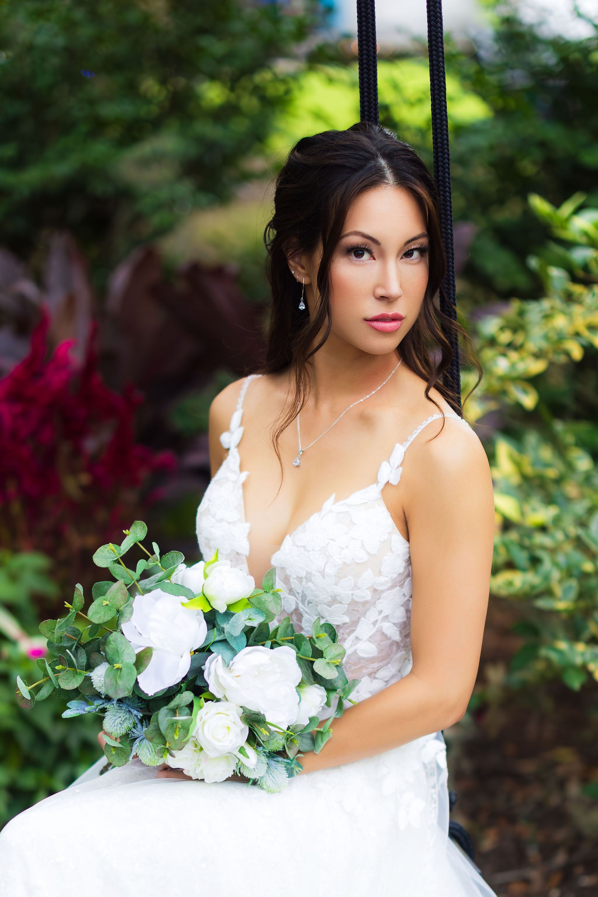 Bride in a white lace dress holding a white-and-green bouquet in a garden setting