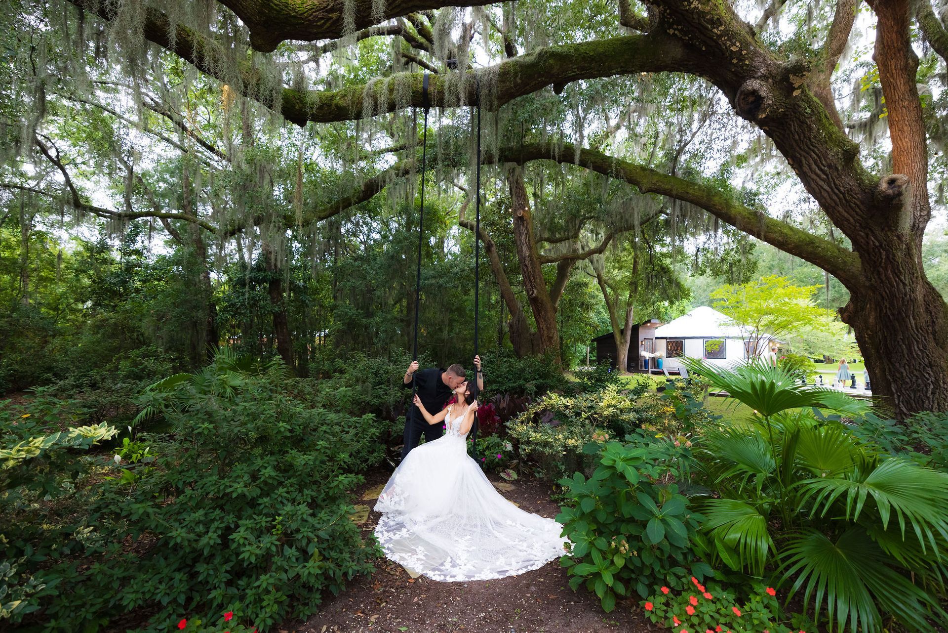 Bride and groom dancing under sprawling trees in a lush garden, bride in a white gown