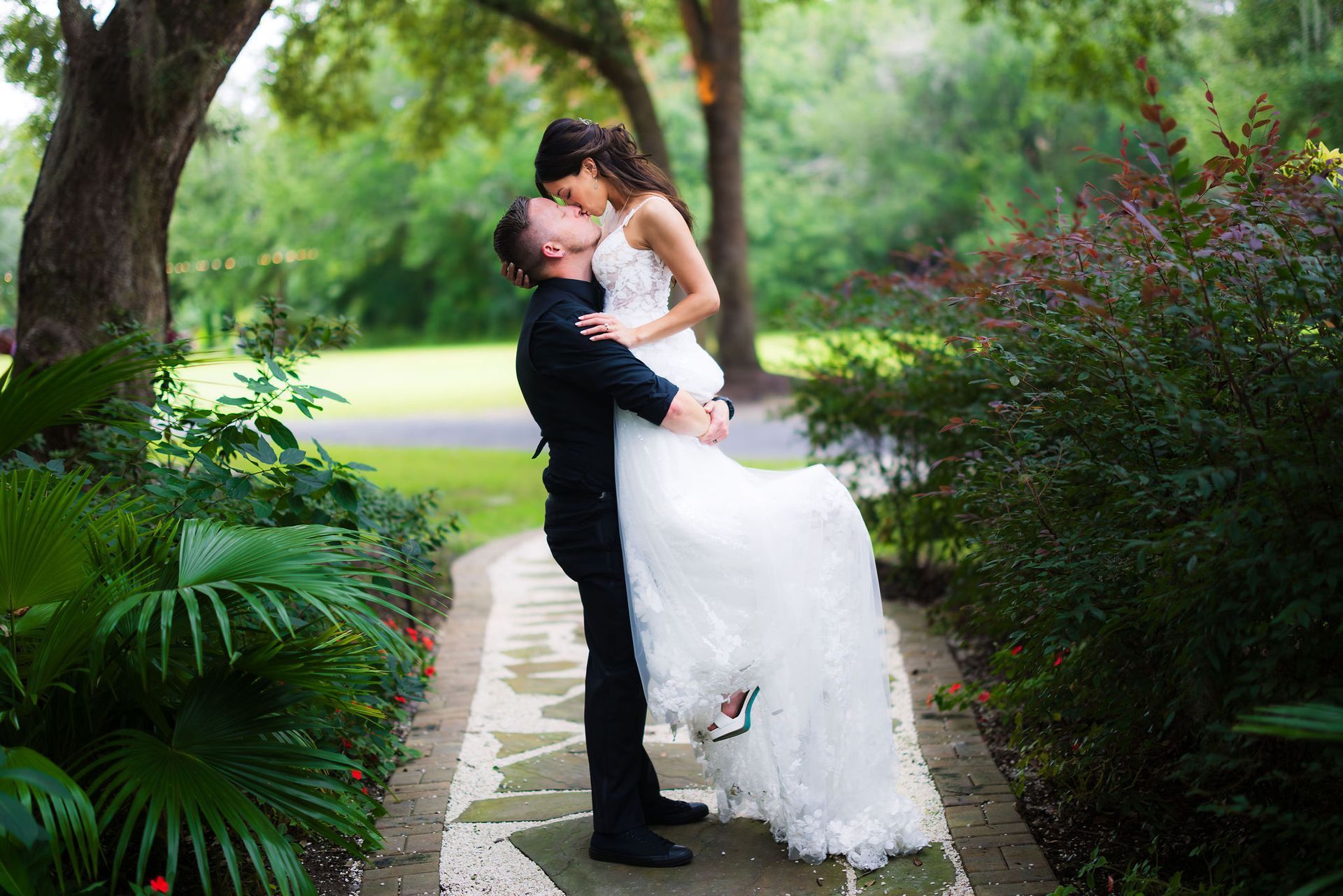 Couple kissing on a garden path, with lush greenery and flowers around them.