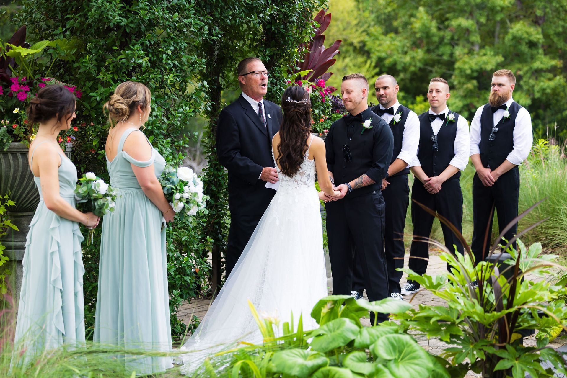 Wedding party standing in a lush garden, with the bride and groom facing attendants in formal attire