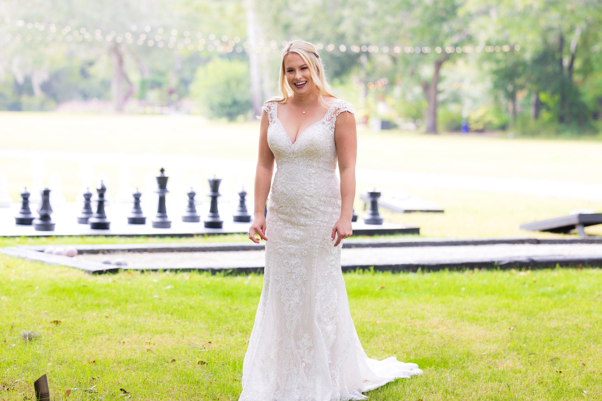 Woman in a white lace dress standing beside oversized chess pieces in a park